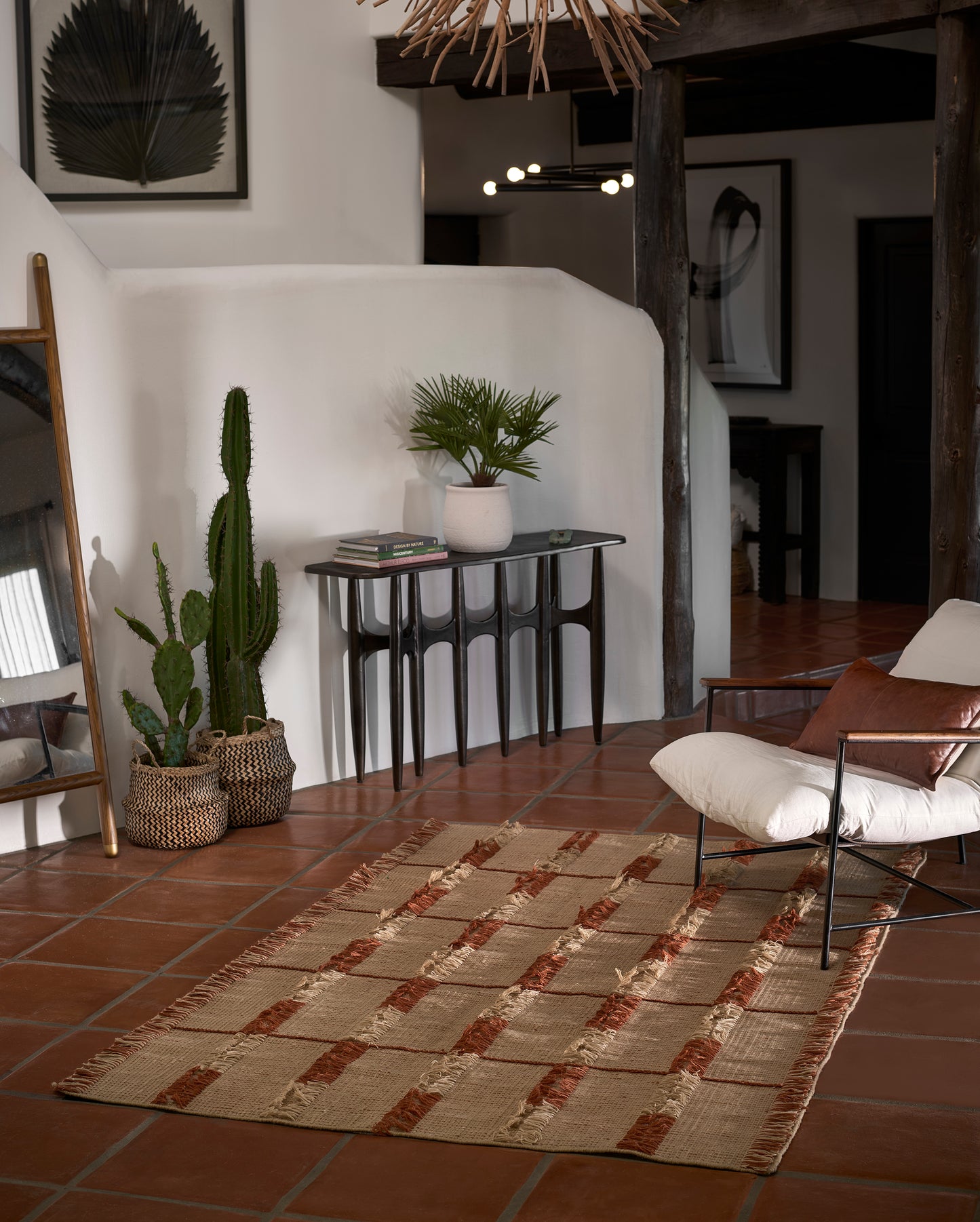 Beige jute rug with rust brown stripes on terracotta tile; boho-living room with woven baskets, cactus, palm, black console.