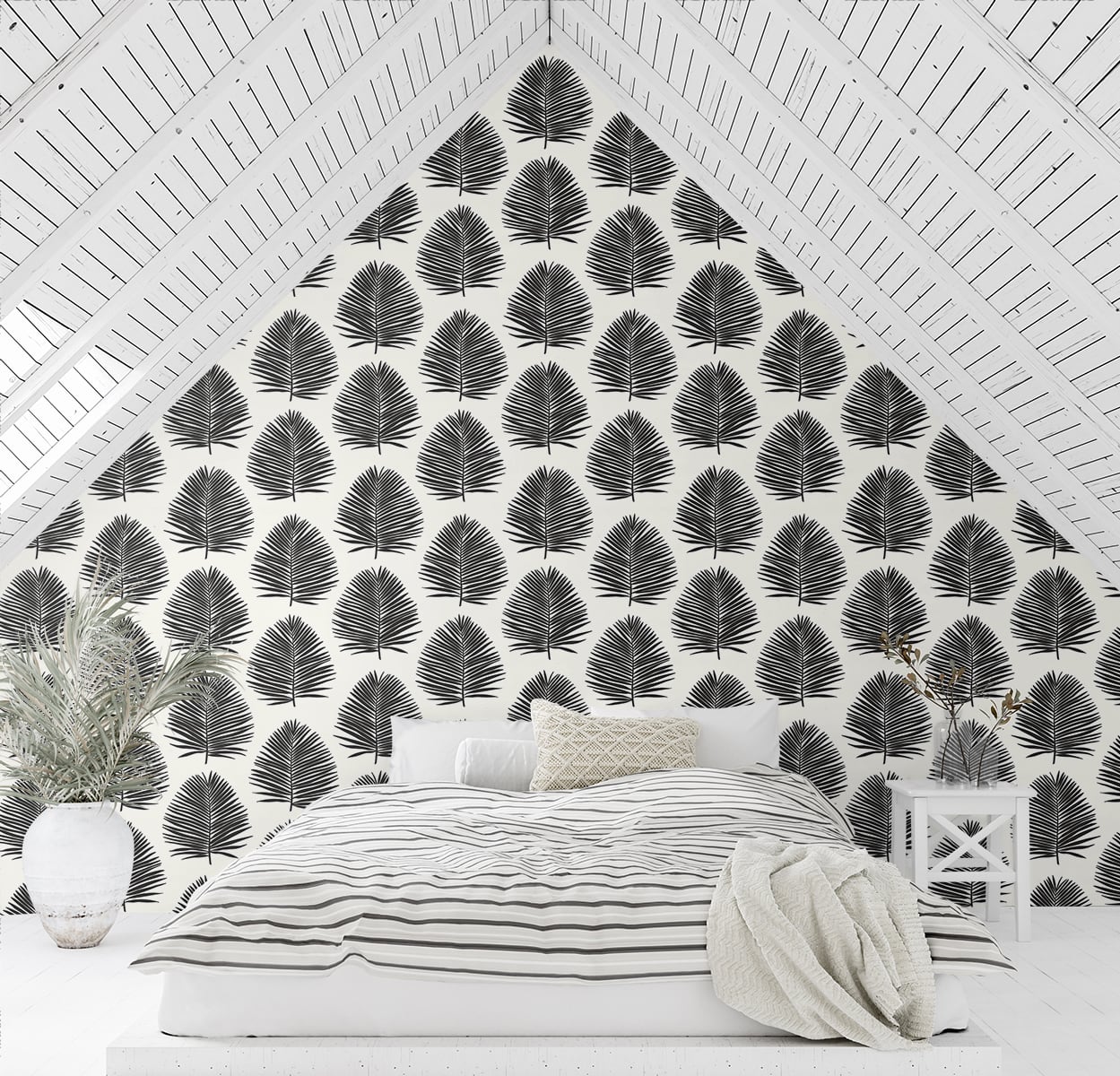White bedroom features black palm-leaf wallpaper on a pitched ceiling, striped bedding, a beige throw and white furniture.