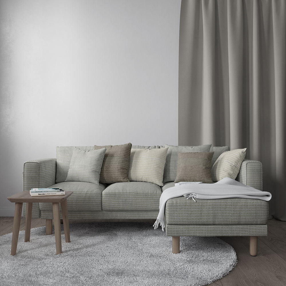 Grey solid fabric upholstered sectional with chaise in a modern living room, with cushions, light throw, wooden side table & rug.