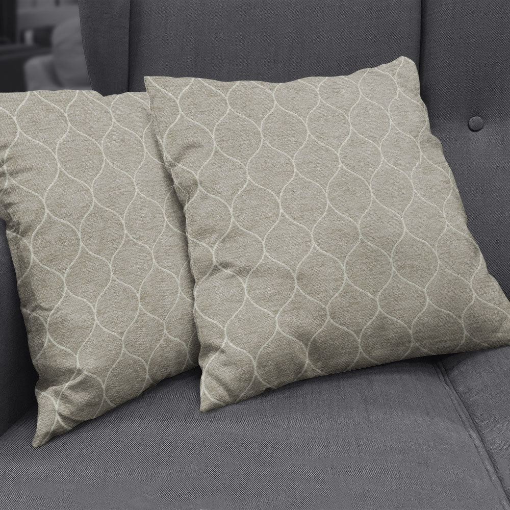 Two beige square decorative cushions with white interlocking curved-line pattern on a dark gray sofa.