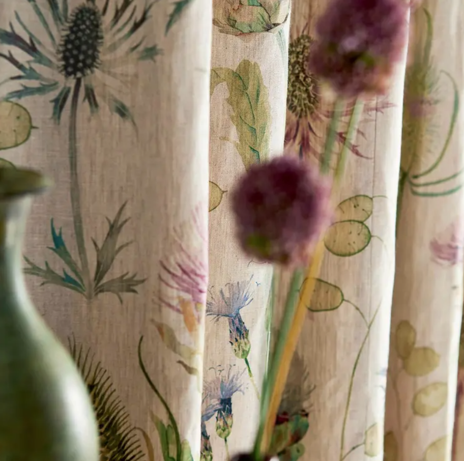 Close‑up of Sanderson Thistle Garden linen fabric (DEBB226423) showing printed thistle and seed‑pod motifs in soft fig tones and natural linen background — ideal for upholstery, draperies, cushions and interior design projects.