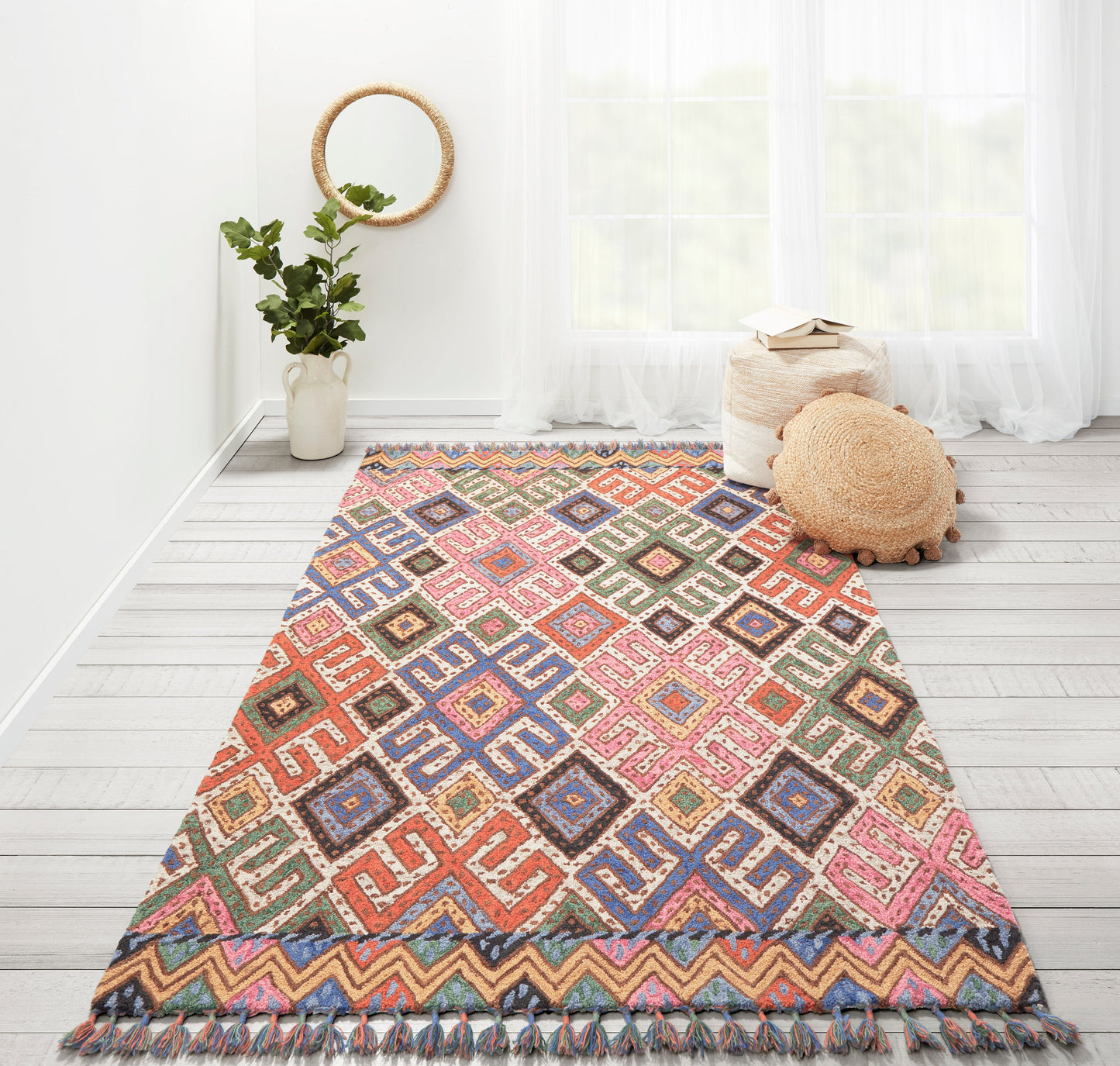 Colorful woven area rug with geometric diamond pattern and fringed ends, placed in a bright airy room.