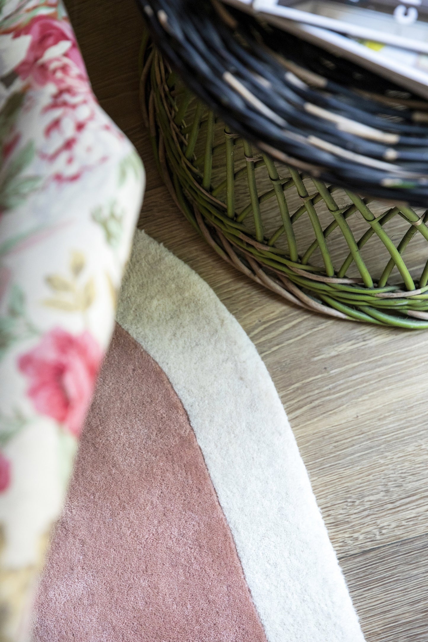 Color-block round rug in pink and cream on wooden floor, with floral fabric draped nearby and a wicker basket.