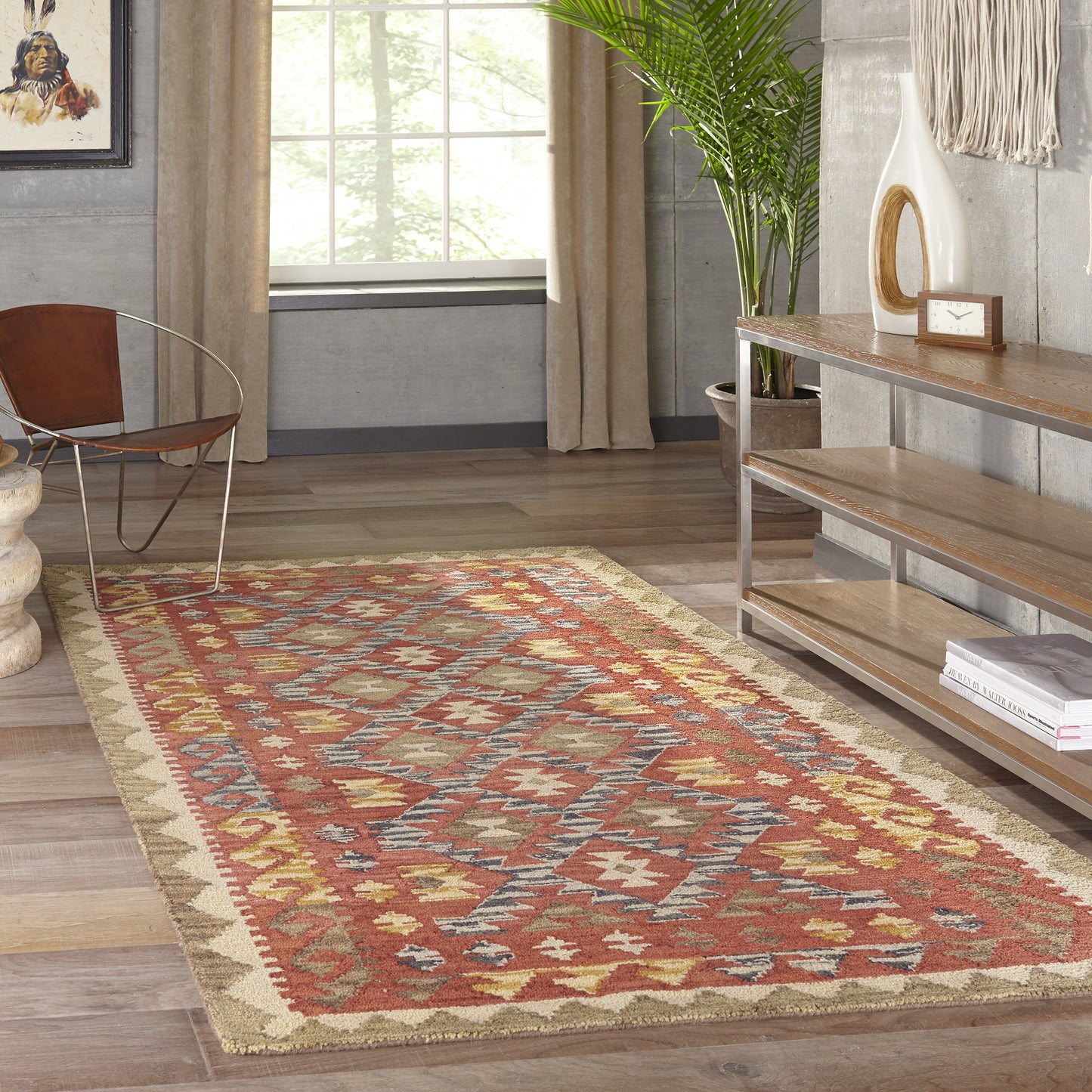 Red geometric area rug with cream border and blue accents on a wood floor, flanked by a metal-framed chair and wooden shelf.