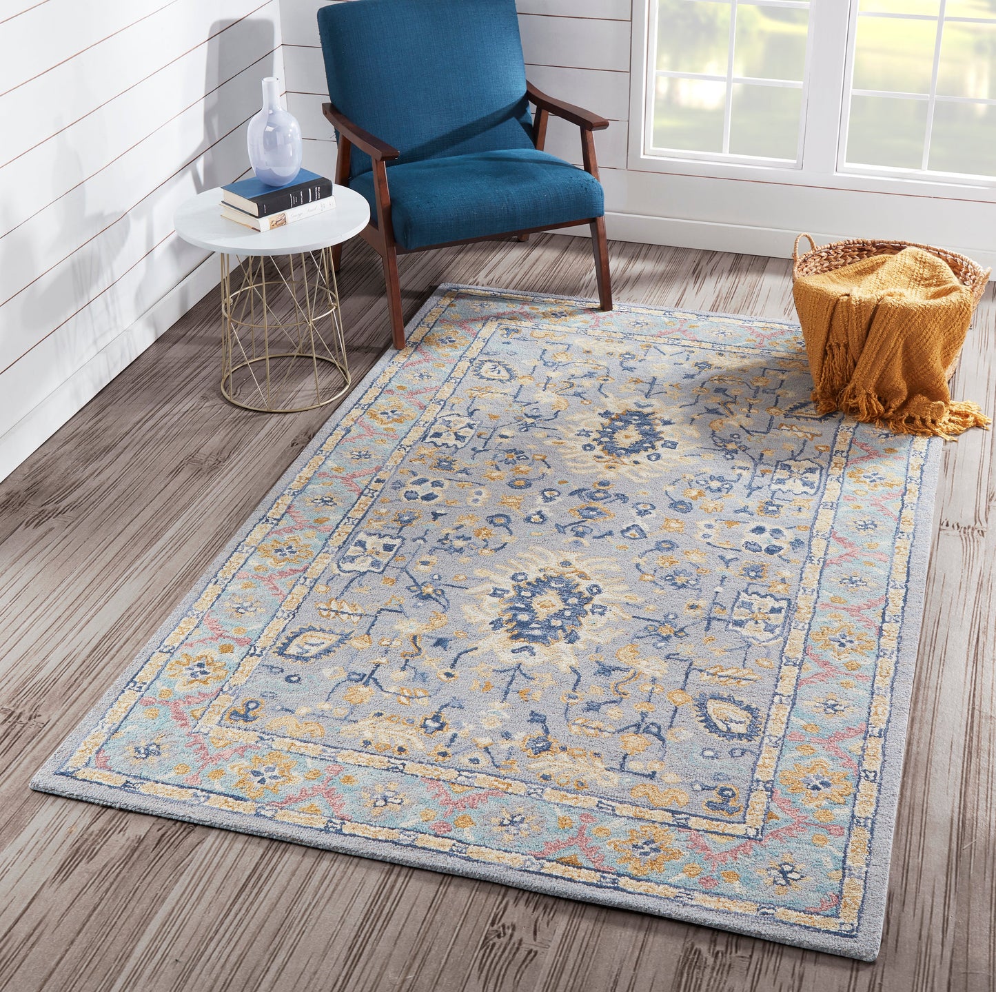Blue upholstered mid-century chair with wooden arms beside a white round side table on a blue-cream oriental rug.
