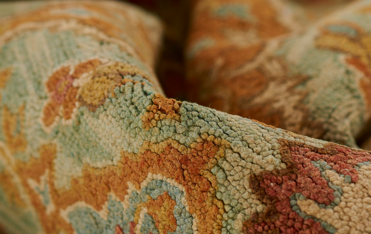 Close-up of a tufted area rug in teal, rust & gold & beige with an ornate pattern and soft wool pile.