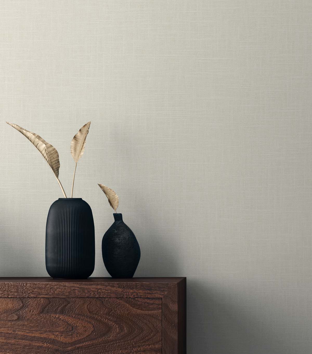 Tall ribbed navy vase with dried leaves beside a small black vase on a wooden dresser against a beige textured wall.
