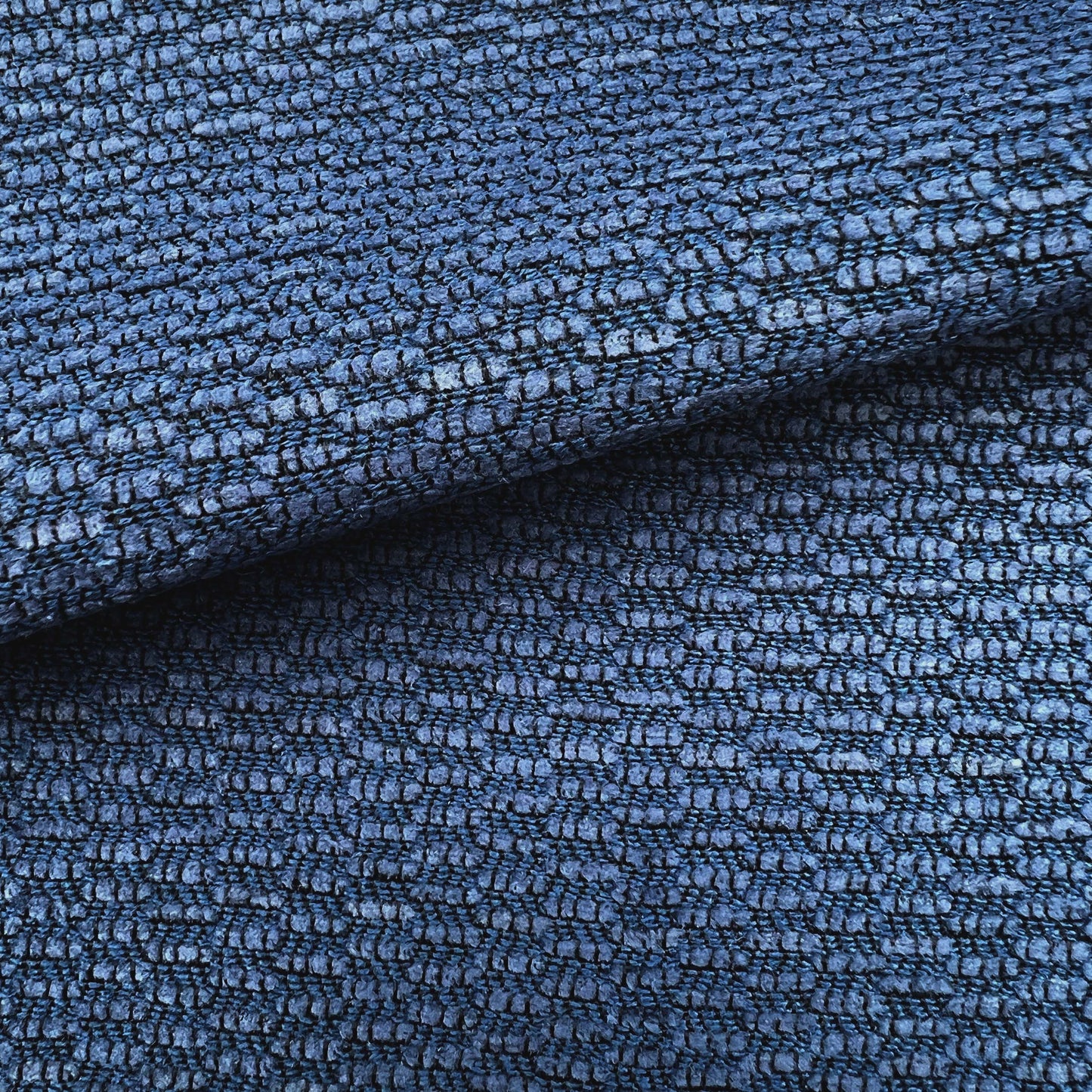 Deep blue textured chenille fabric with a pebble-like weave and folded edge, suitable for upholstery or outdoor use.