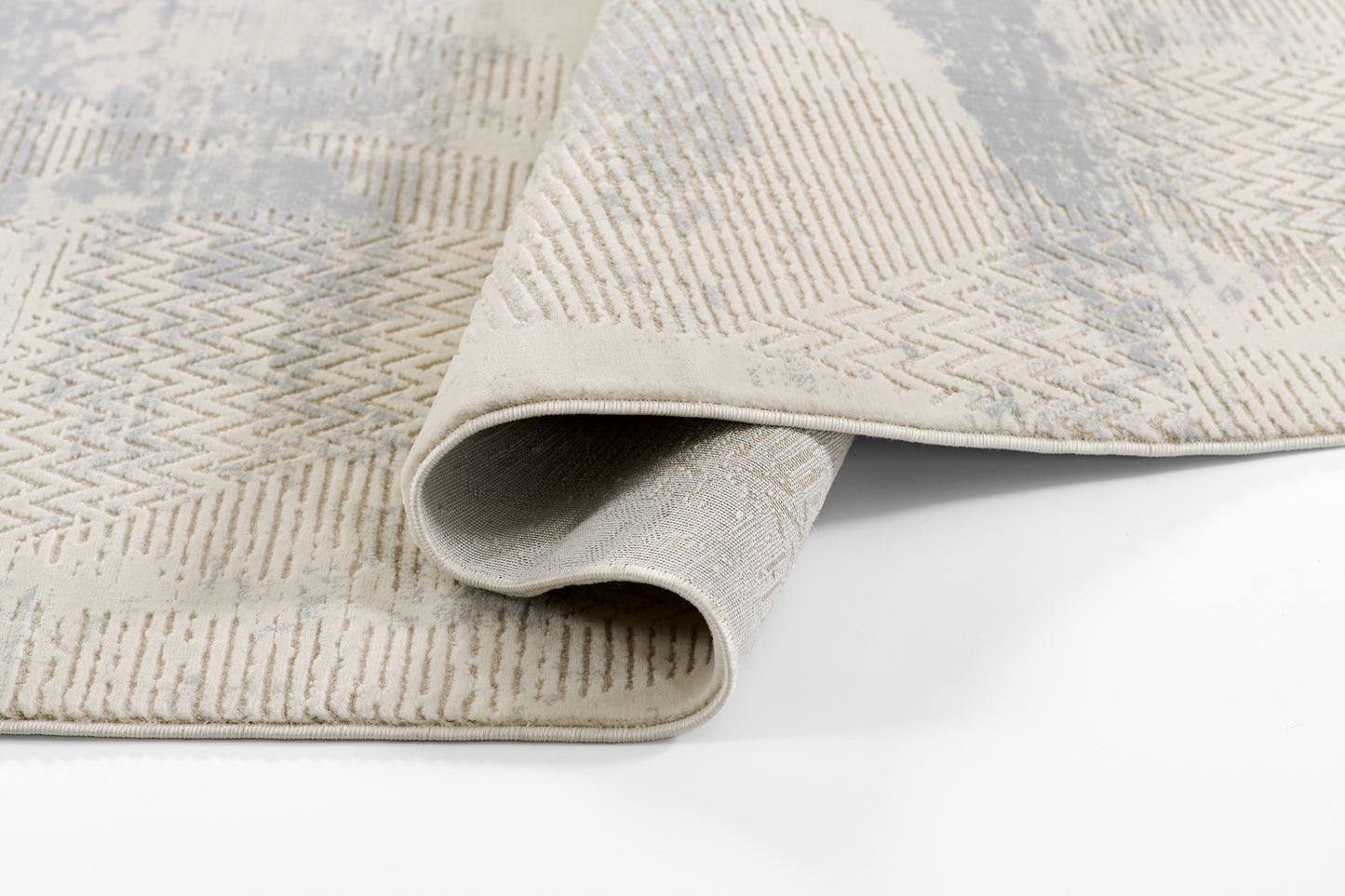 Beige and cream geometric rug with chevron pattern, woven texture, folded edge revealing soft backing.