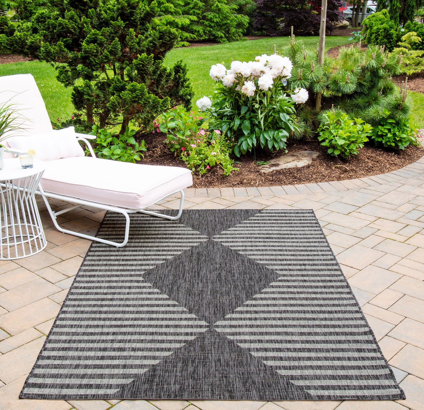 Outdoor runner rug with charcoal and light gray striped diamonds on a brick patio beside a white lounge chair.