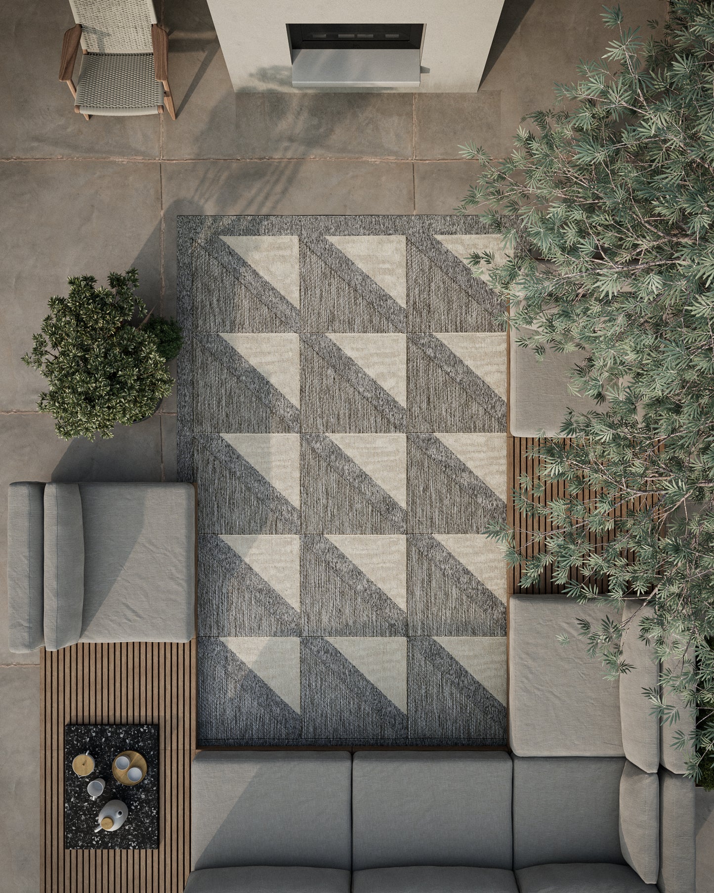 Outdoor rug with dark and light gray geometric triangles, rectangular, on a concrete patio beside a gray sectional.