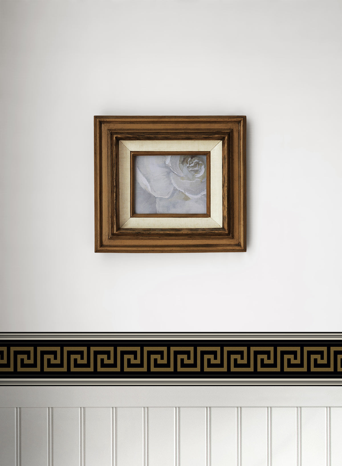 Square brown wood frame with cream mat and grayscale rose print, mounted above a Greek key border on a white wall.