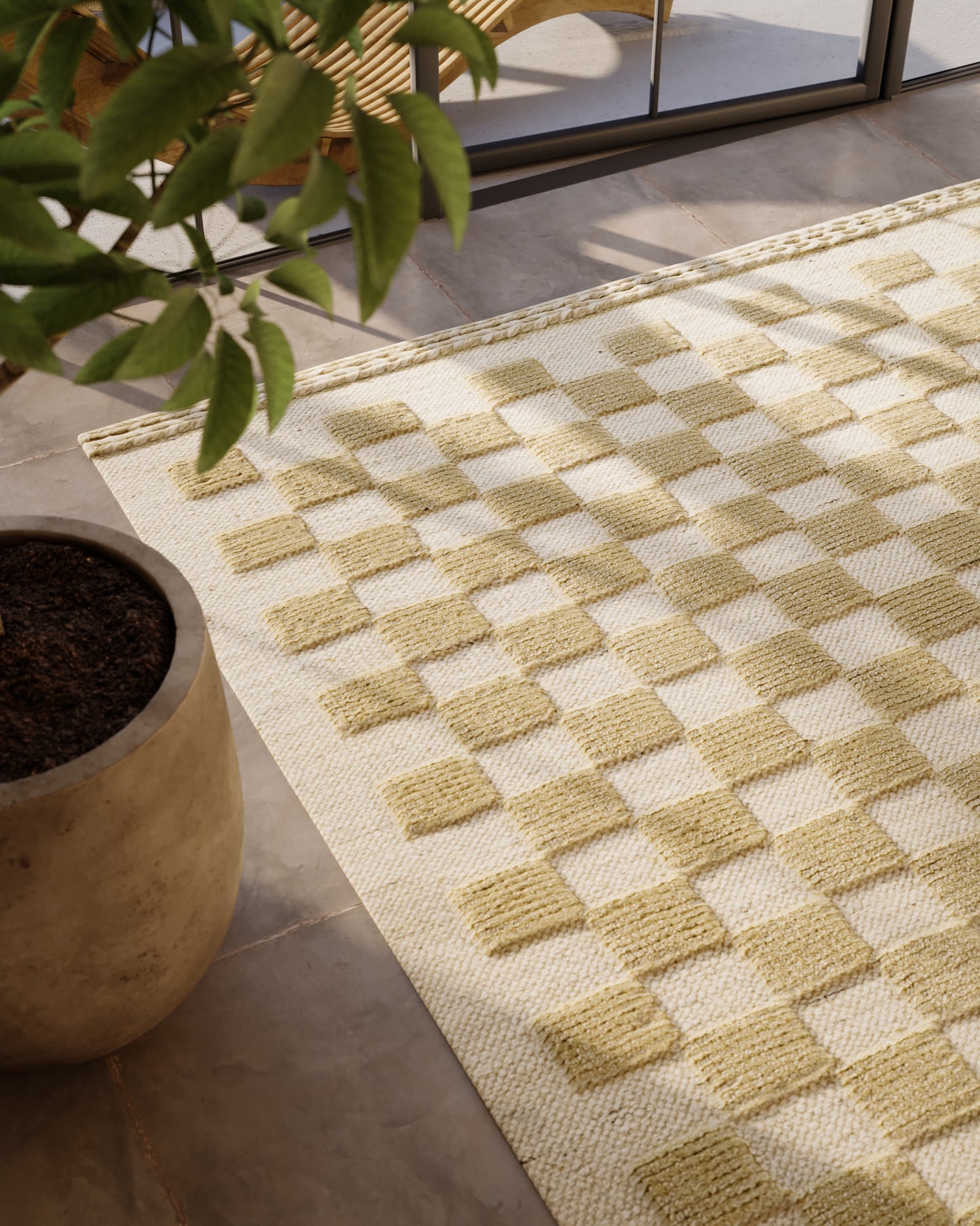 Beige and ivory checker rug on a light floor beside a large potted plant by a glass window.
