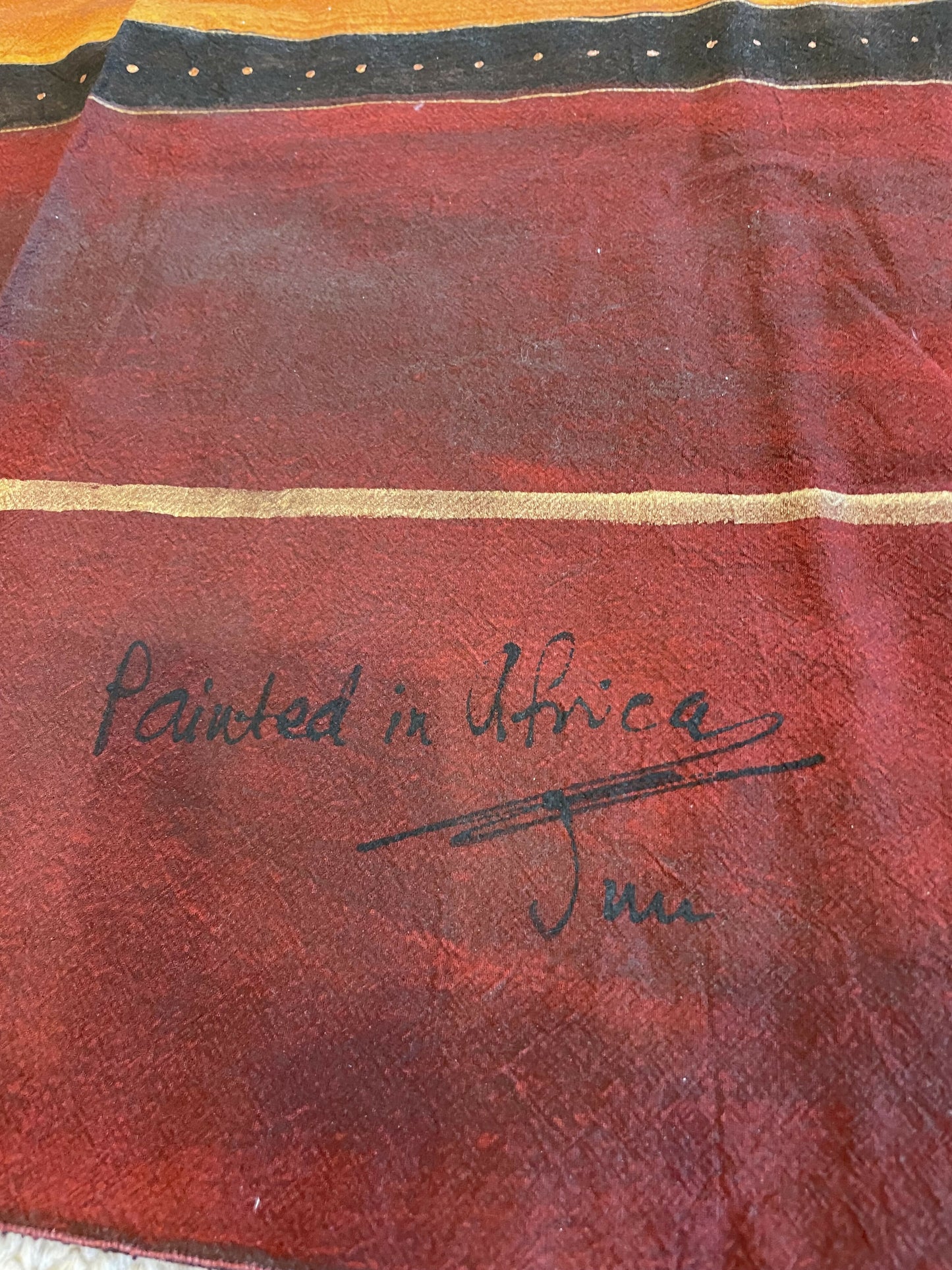 Red and orange fabric with black and gold stripes, featuring a signature that reads "Painted in Africa.
