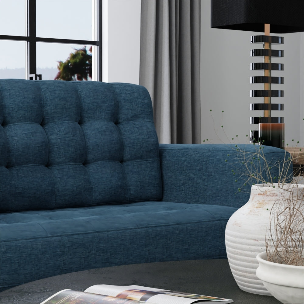 Indigo solid fabric upholstery on a blue tufted sofa in a modern living room, with a tall stacked-ring lamp and a white ceramic vase on a coffee table
