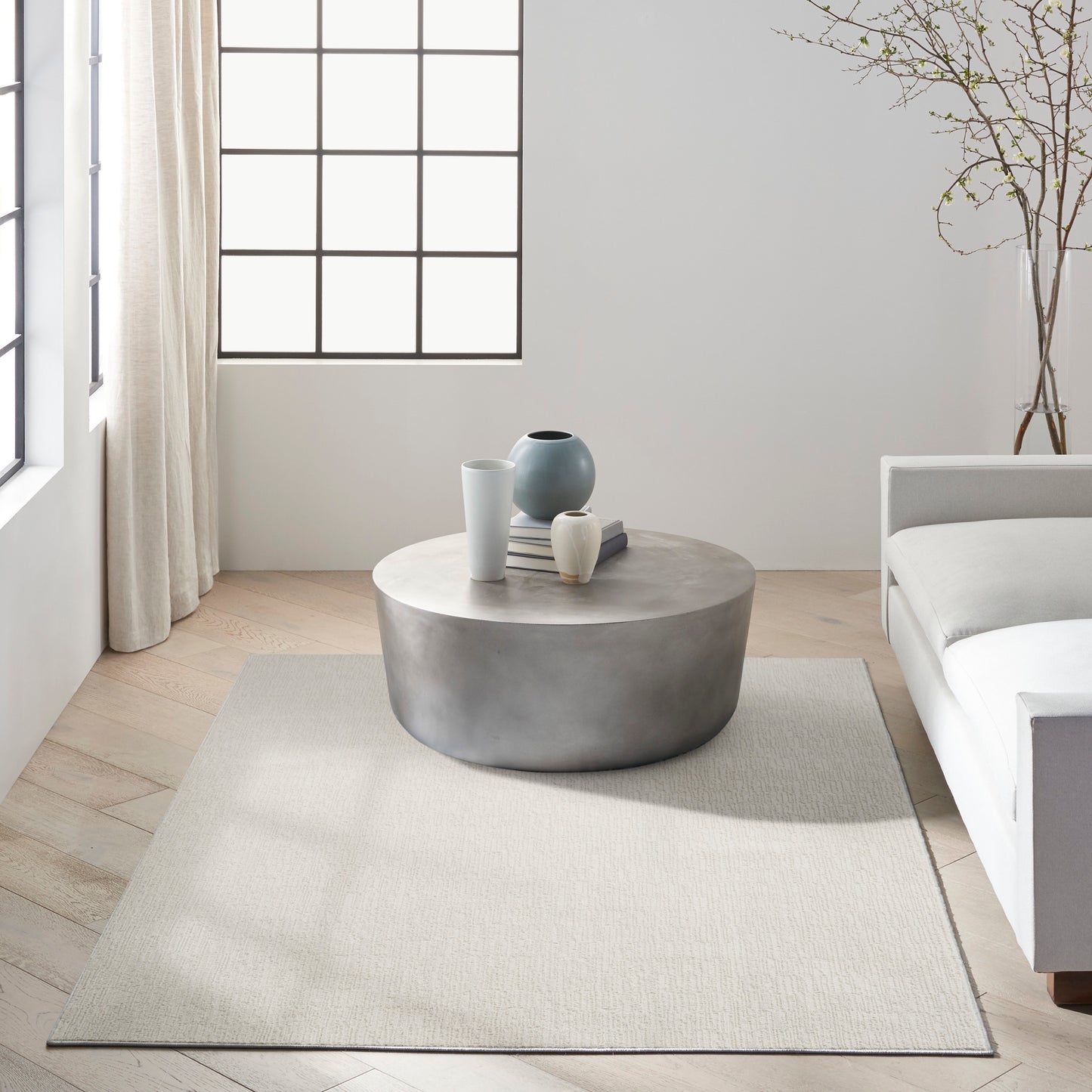 Round concrete coffee table with white & blue vases and stacked books on a light rug in a neutral minimalist living room.