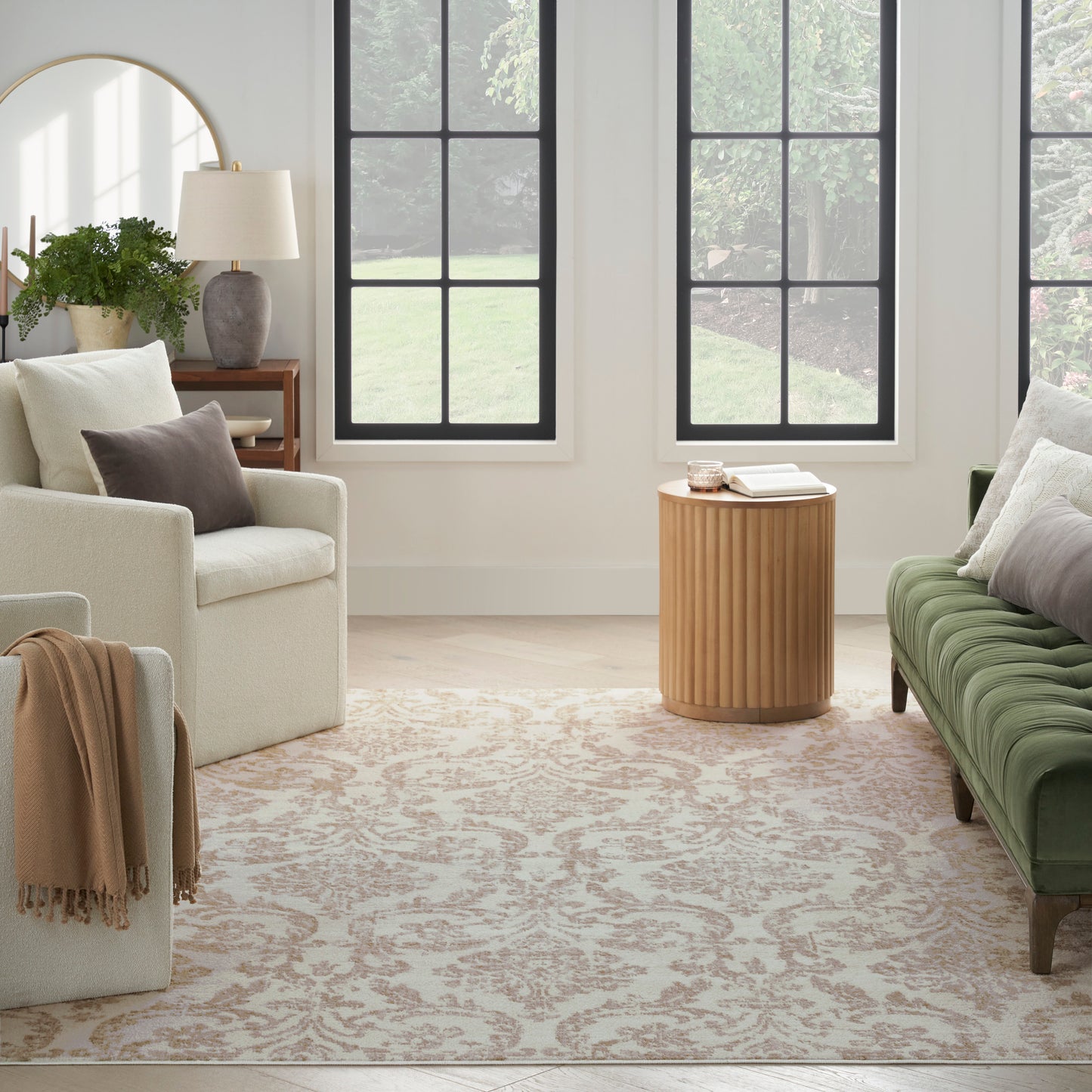 Modern living room with cream sofa, green velvet tufted sofa, round wooden side table, beige rug, black-framed windows.
