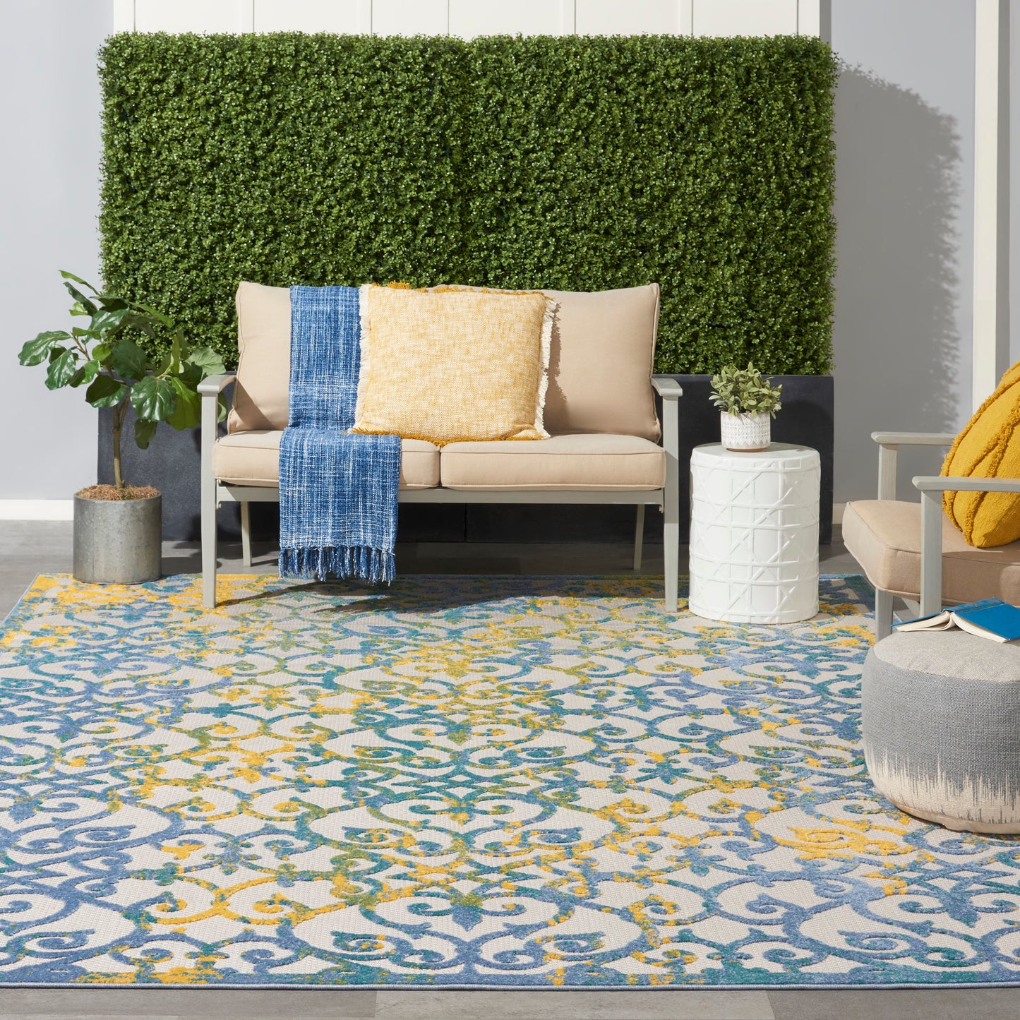 Indoor area rug with blue and yellow ornate motif on light gray; beige sofas, blue throw, yellow cushions.