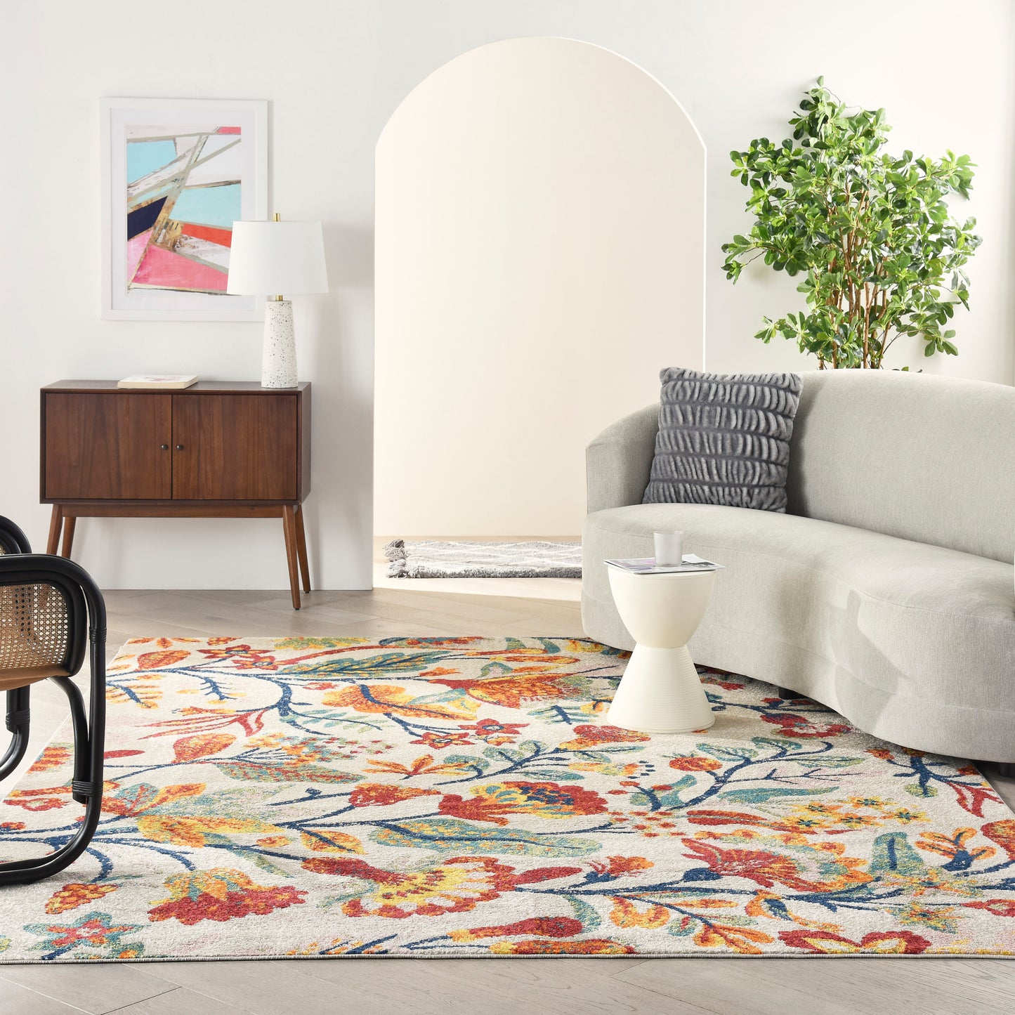 Cozy contemporary living room with floral rug, gray sofa, white coffee table, wooden console, abstract art, and a plant.