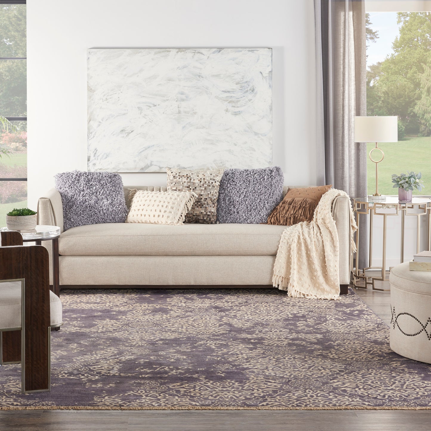 Beige sofa with purple & beige pillows, cream throw, marble wall art above, purple patterned rug, cozy living room.