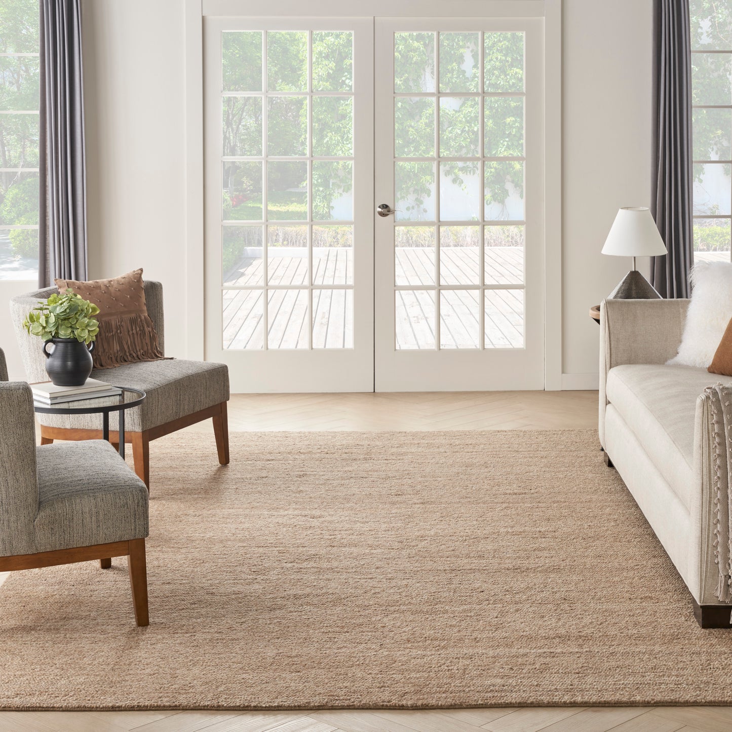 Living room scene featuring natural jute rug, gray upholstered chairs, round black metal side table with plant, beige sofa.