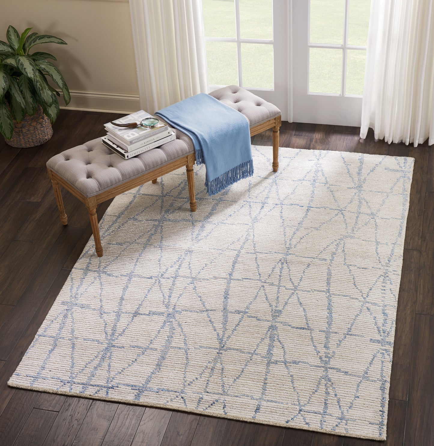 Cream flat-weave area rug with pale blue geometric lattice in a living room beside a tufted beige bench and blue throw.