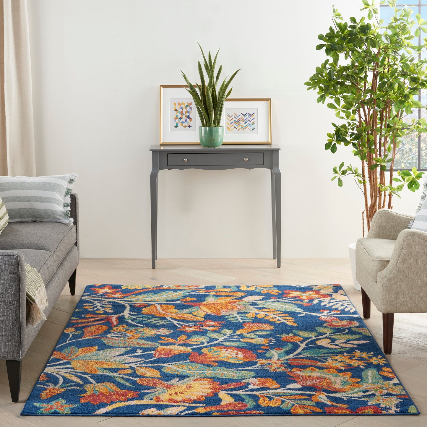 Rectangular blue floral area rug with orange and beige accents on a light wood floor in a modern living room.