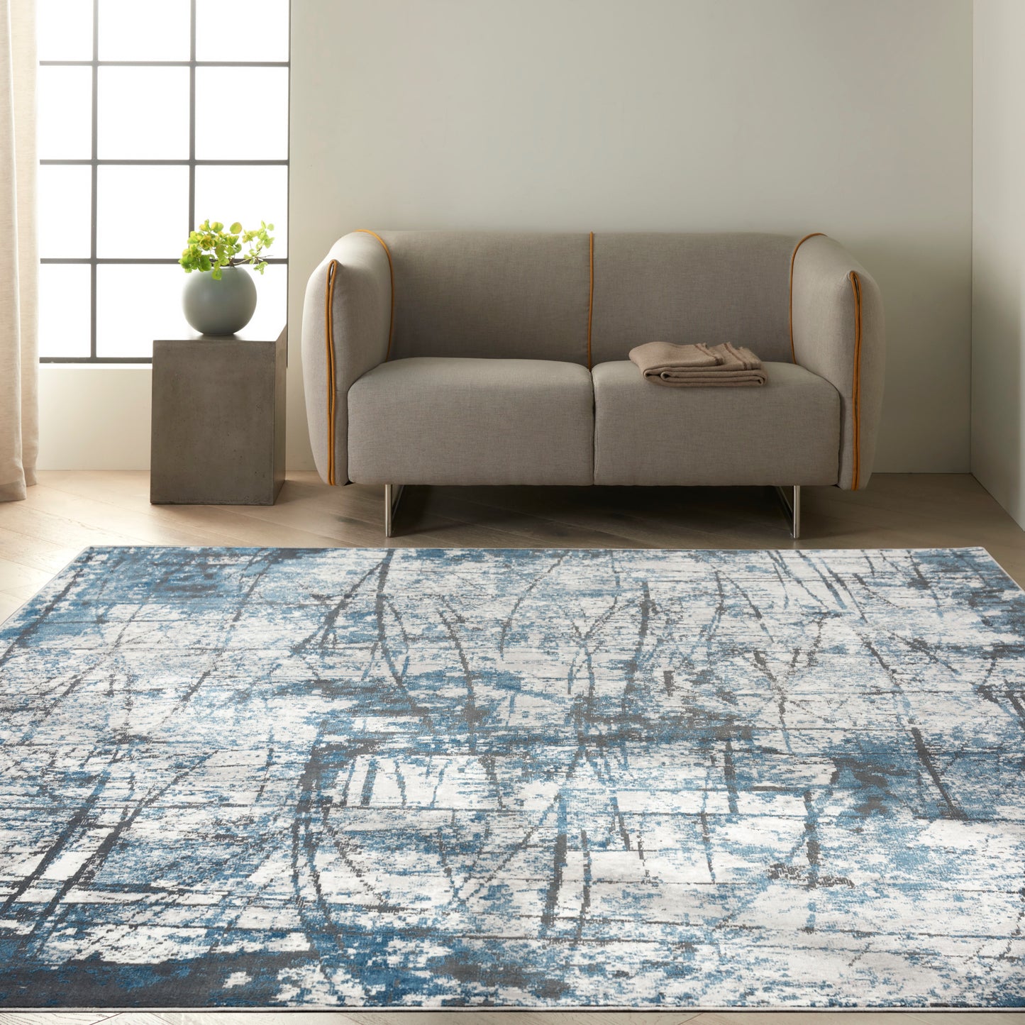 Gray fabric sofa with orange piping and metal legs, folded beige throw, on a blue-gray abstract rug in a modern living room.