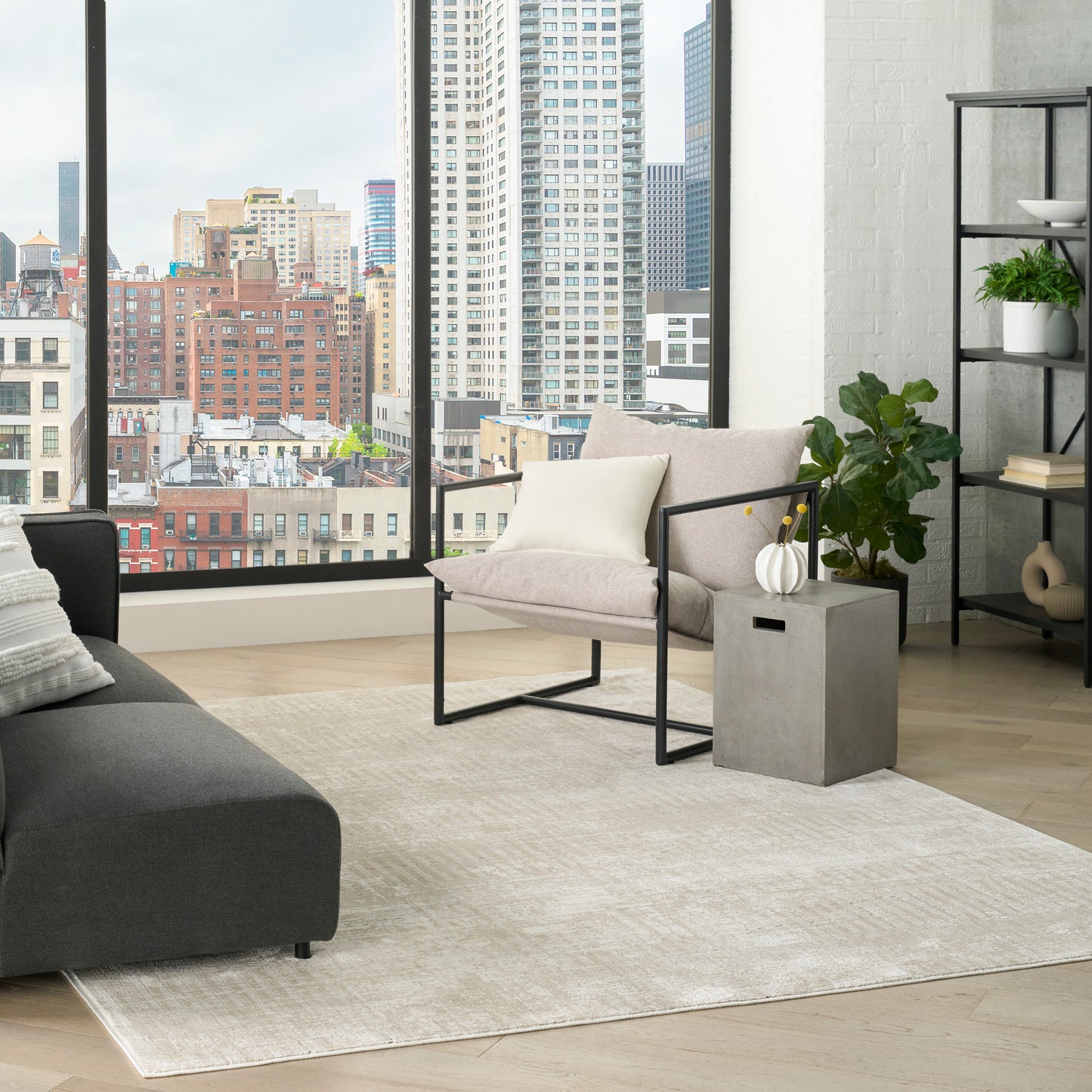 Modern city-view living room with beige fabric armchair on a black metal frame, dark gray sofa, light rug, concrete table.