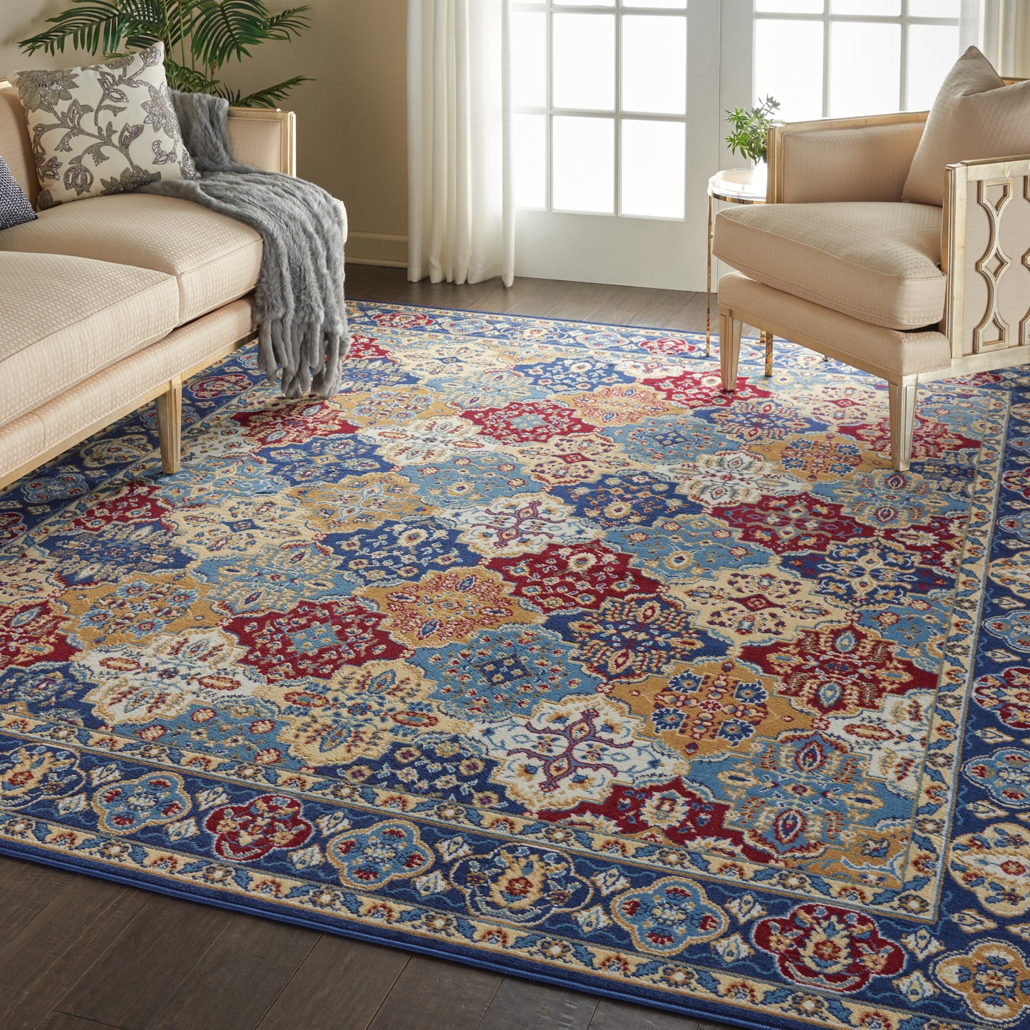 Ornate multicolor oriental area rug with blue, red, gold and ivory motifs on dark wood floor, flanked by beige sofas.
