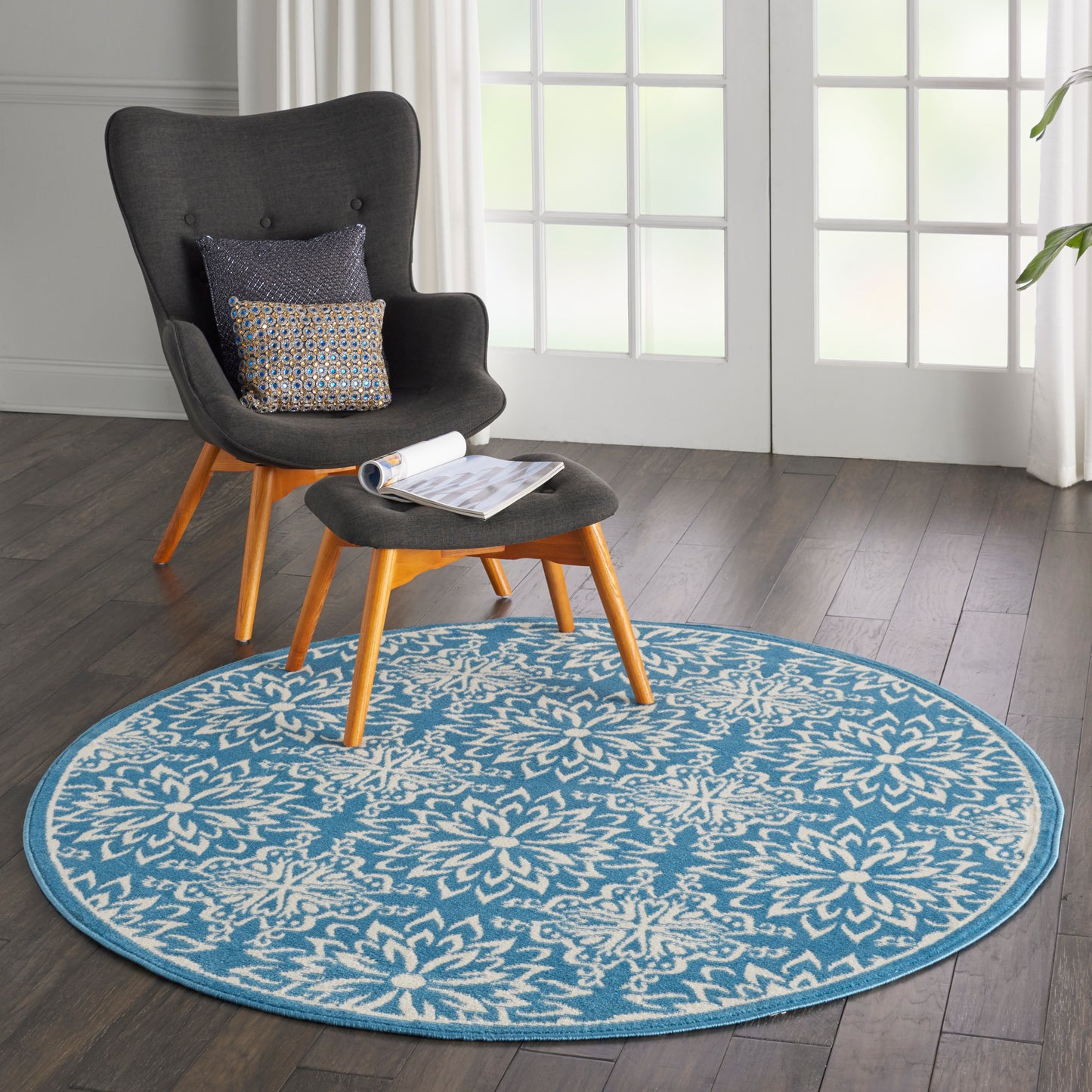 Round blue and white floral rug under a dark gray modern lounge chair with wooden legs and matching ottoman, reading nook.