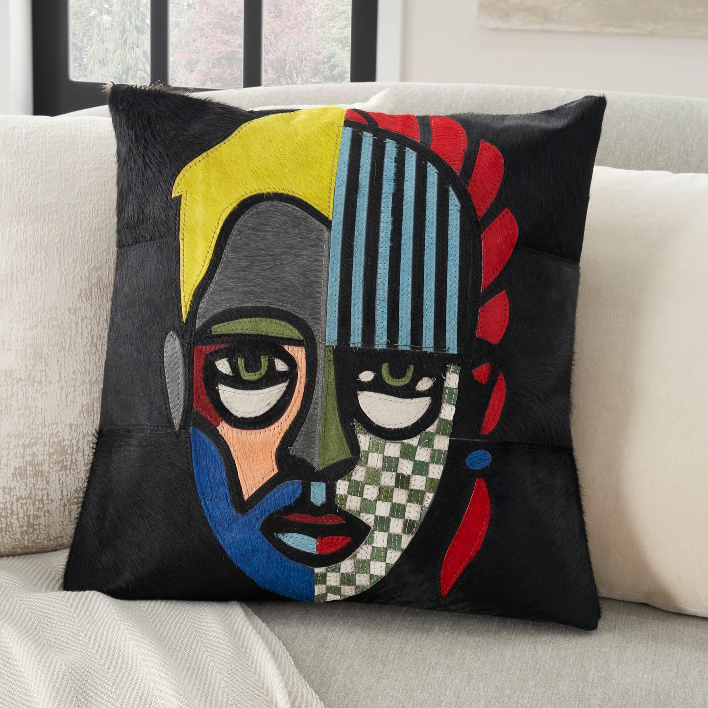 Black square throw pillow with yellow patch, blue stripes and red petal motif on a sofa.