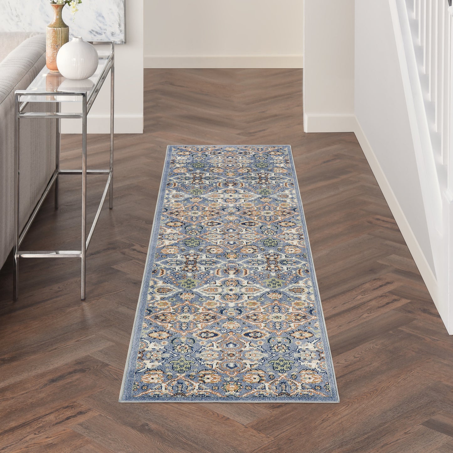 Blue oriental runner rug with cream and gold motifs on dark herringbone hallway floor beside a metal-glass console table.