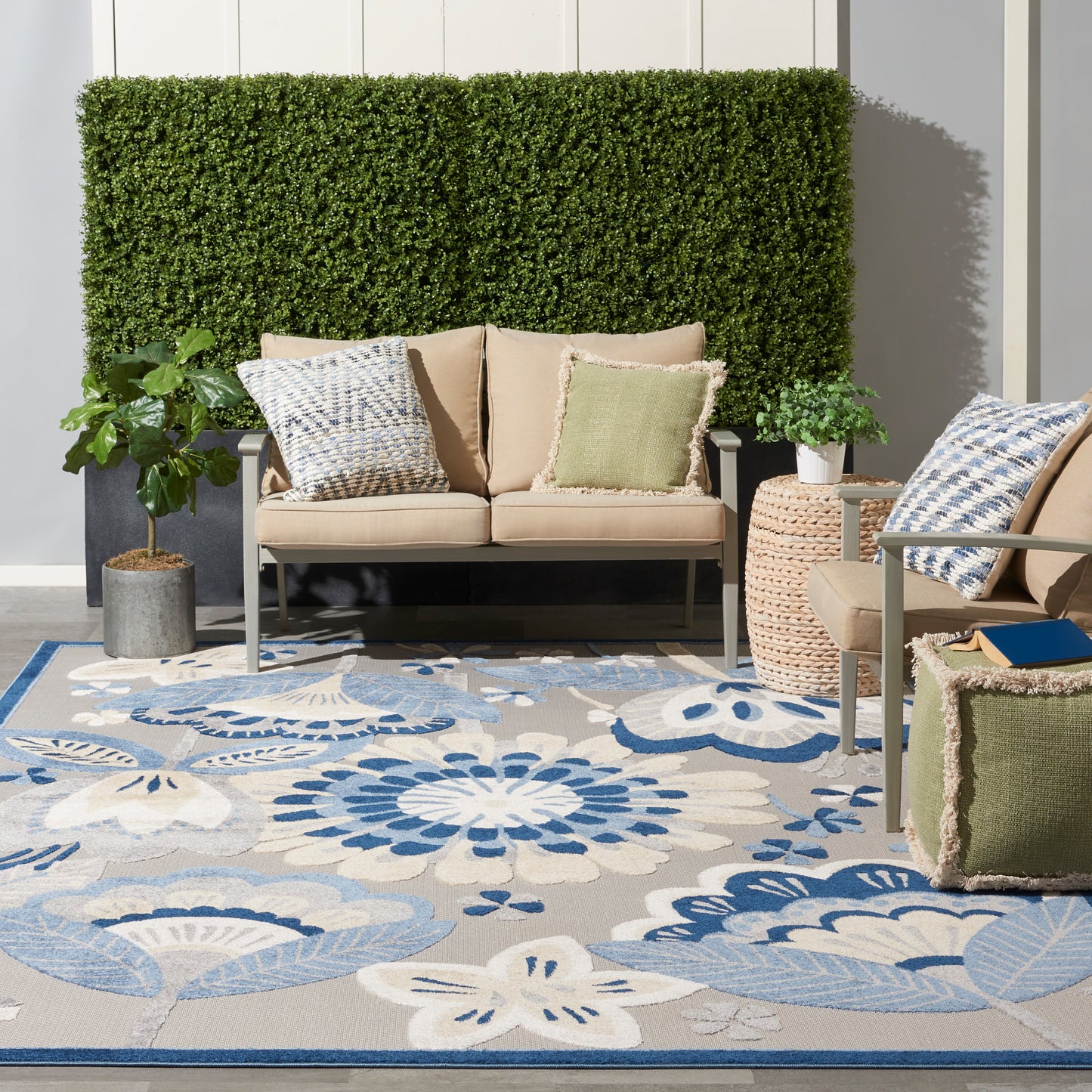 Blue floral outdoor rug on a patio with a beige metal-frame sofa, green patterned cushions, and potted plants.