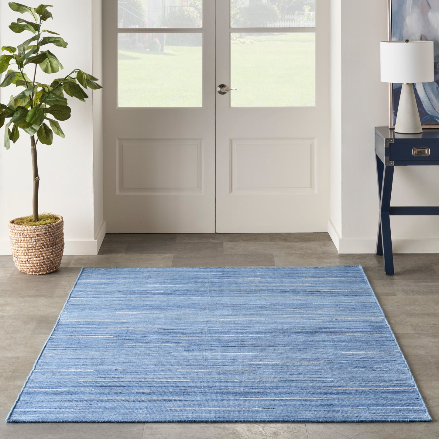 Blue striped flatweave entryway rug on wood floor, with potted plant and console table by double doors.