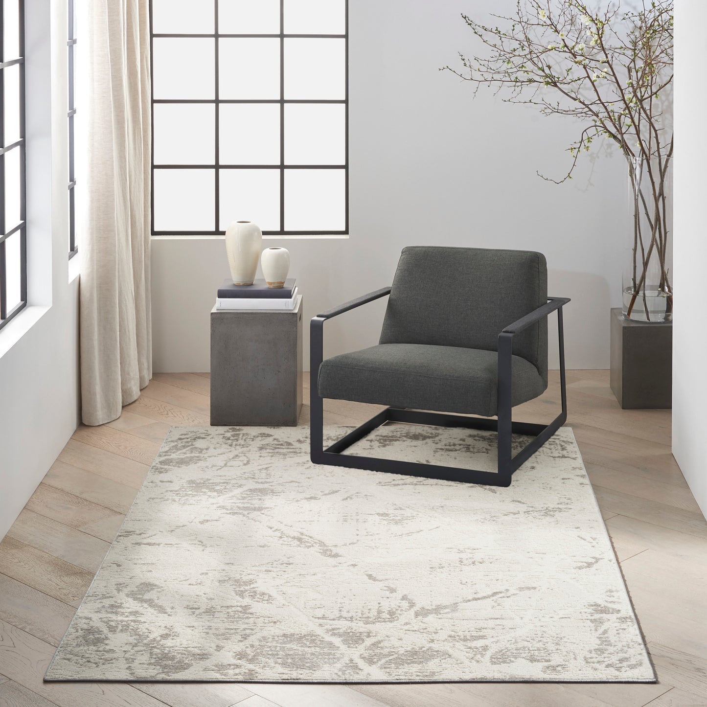 Gray cushioned lounge chair with a black metal frame on a light patterned rug in a bright minimalist living room.