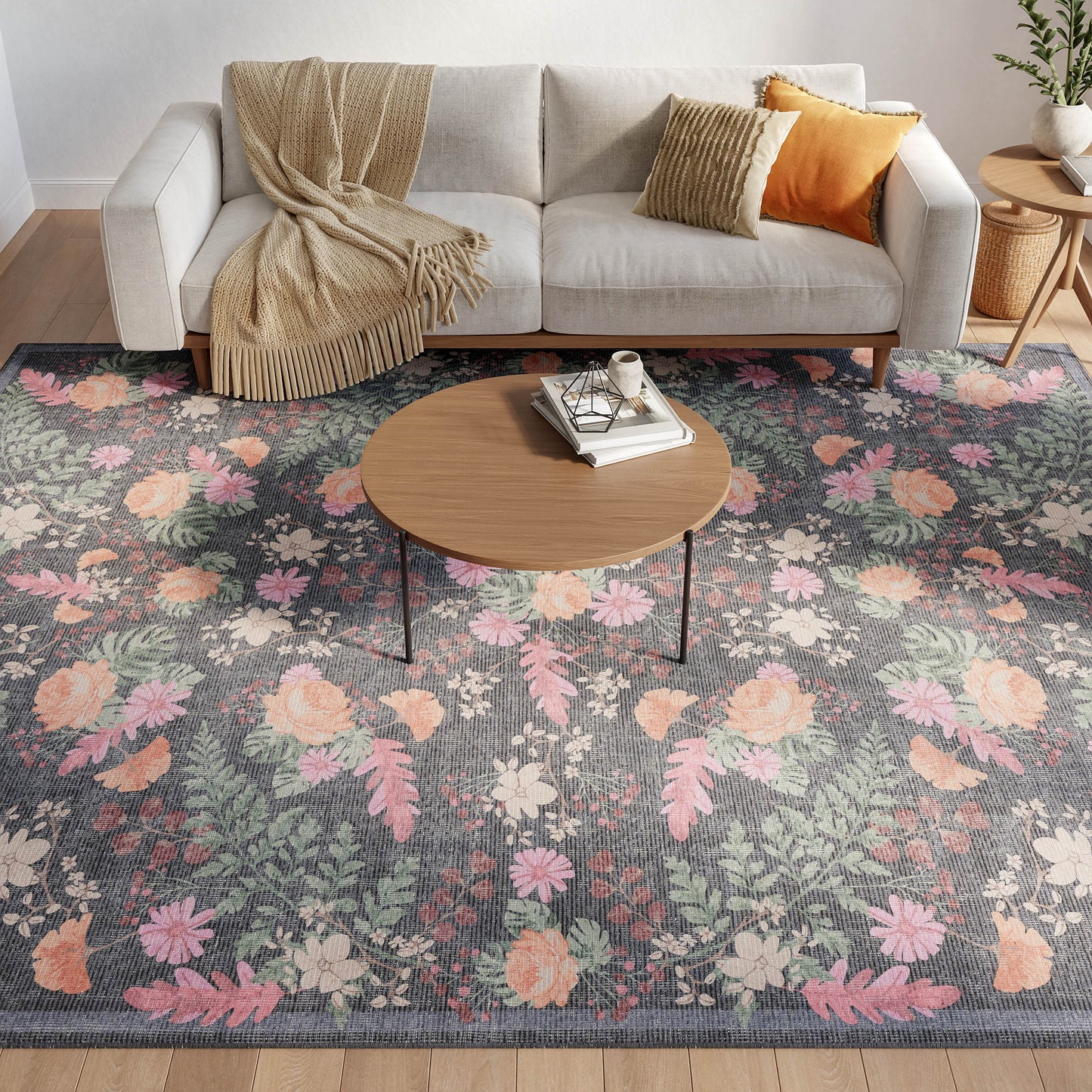 Gray floral area rug with pink, peach and green blossoms beneath a round wood coffee table beside a beige sofa.