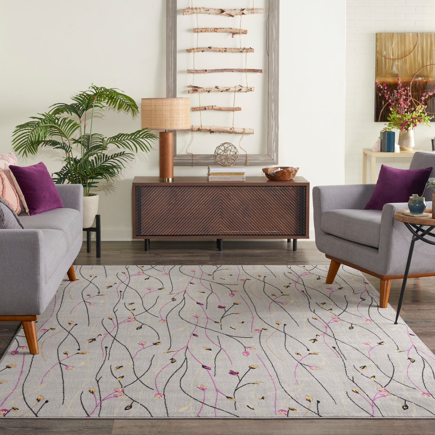 Living room with a light gray patterned rug, mid-century wood console, two gray armchairs with purple cushions.