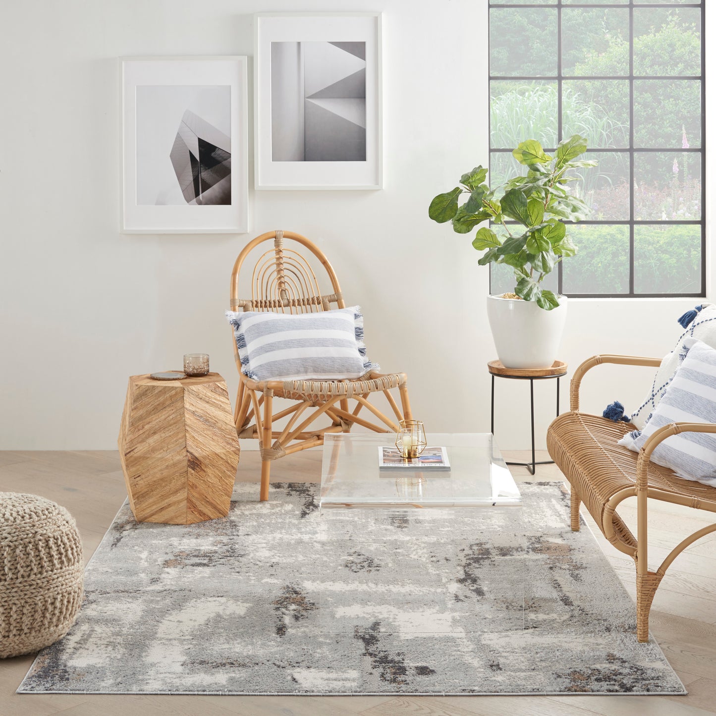 Modern 5' x 7' rug on the floor of a coastal living room with rattan chairs, blue-white striped cushions, glass coffee table, plant, and abstract wall art.