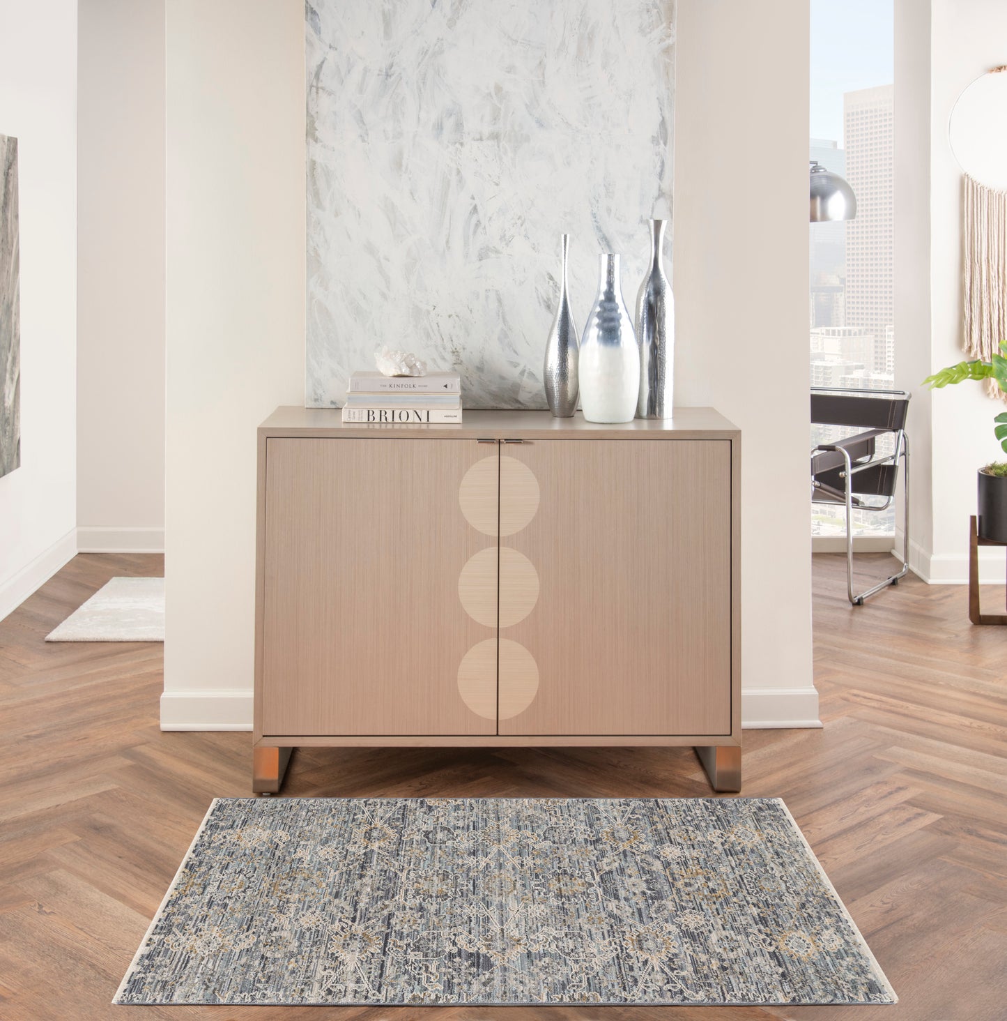 Blue patterned rug, 3' x 5', on the floor in a room setting with light wood furniture, decorative vases & books.