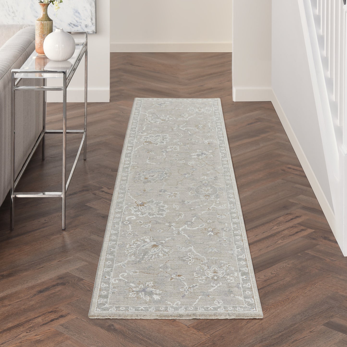 Light gray oriental-style hallway runner rug with ivory floral border on dark brown herringbone wood floor.