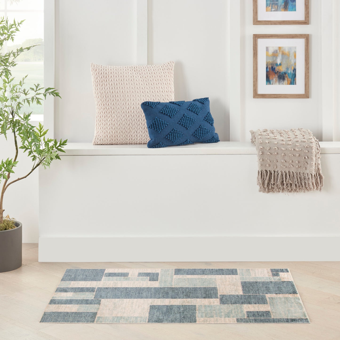 White built-in bench with cream knitted cushion, blue geometric pillow, beige fringe throw, and blue-cream rug.