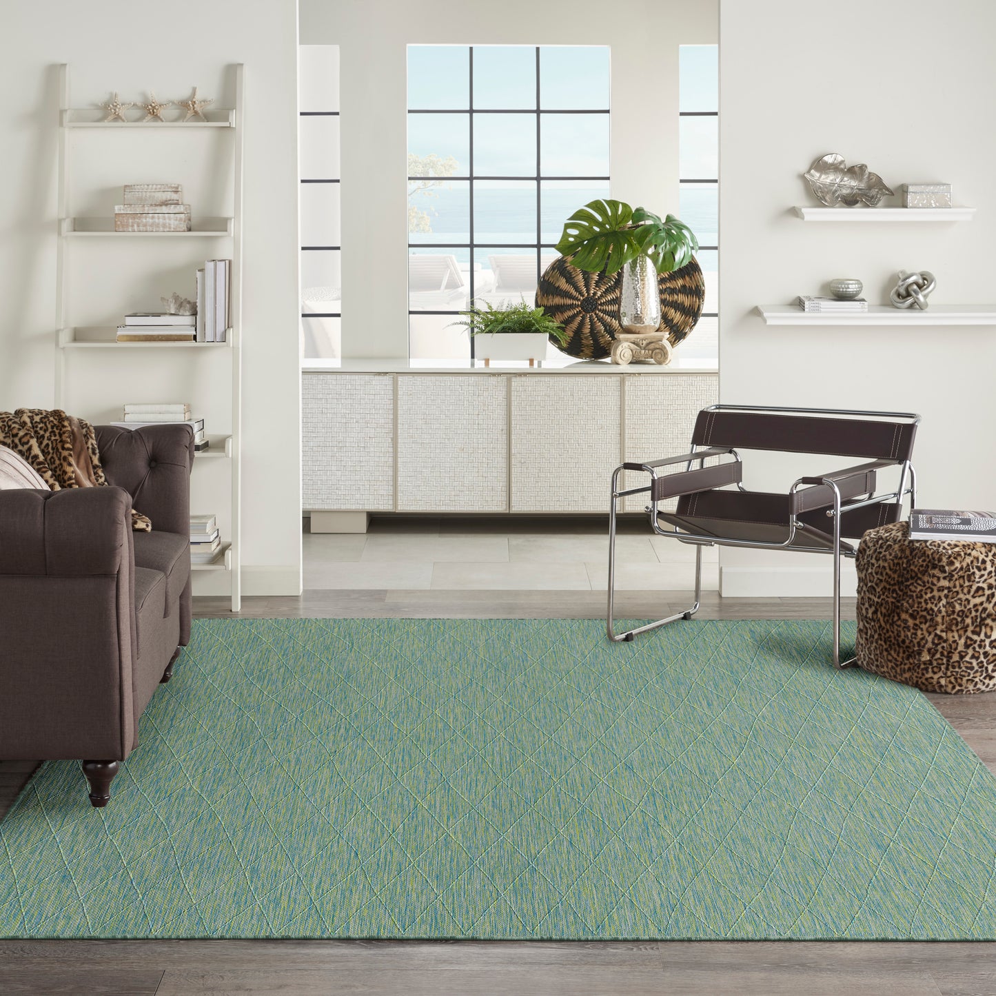 Teal green area rug with subtle diagonal pattern in a modern living room, with brown sofa and metal-framed lounge chair.