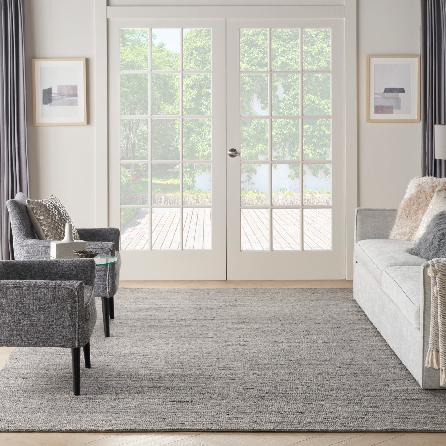 Modern gray living room: light gray sofa, two charcoal armchairs, glass side table, textured rug, white French doors.