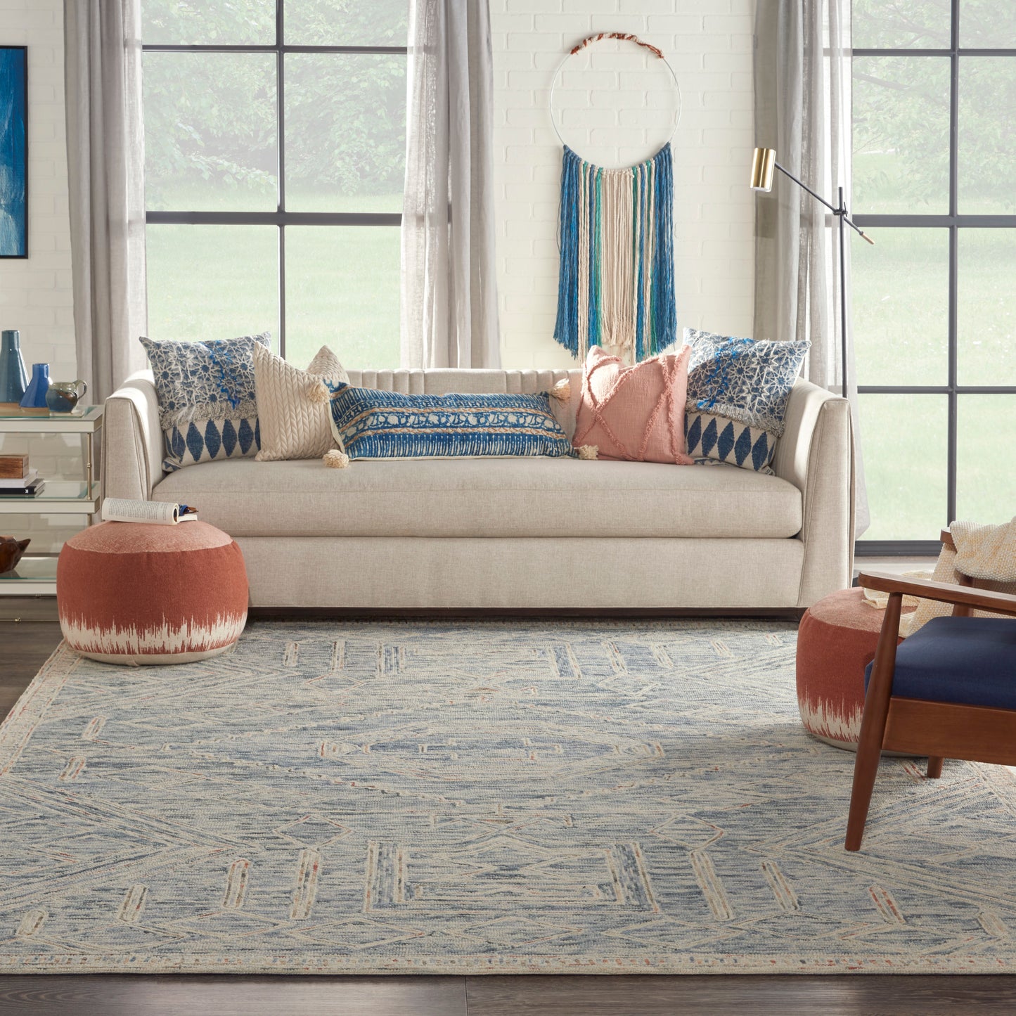 Boho living room with beige sofa, blue patterned cushions, pink accent pillows, blue rug, round coral poufs, wall weave.