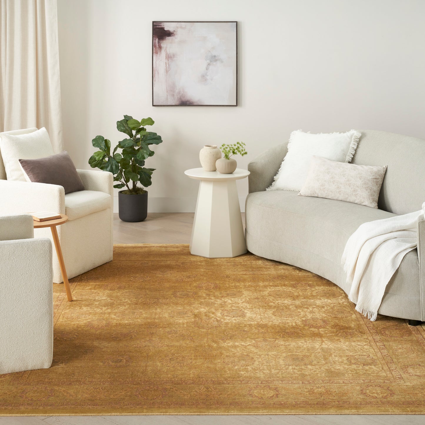 Neutral living room with cream sofas, beige cushions, a gold rug, white geometric side table, wall art, and a potted plant.