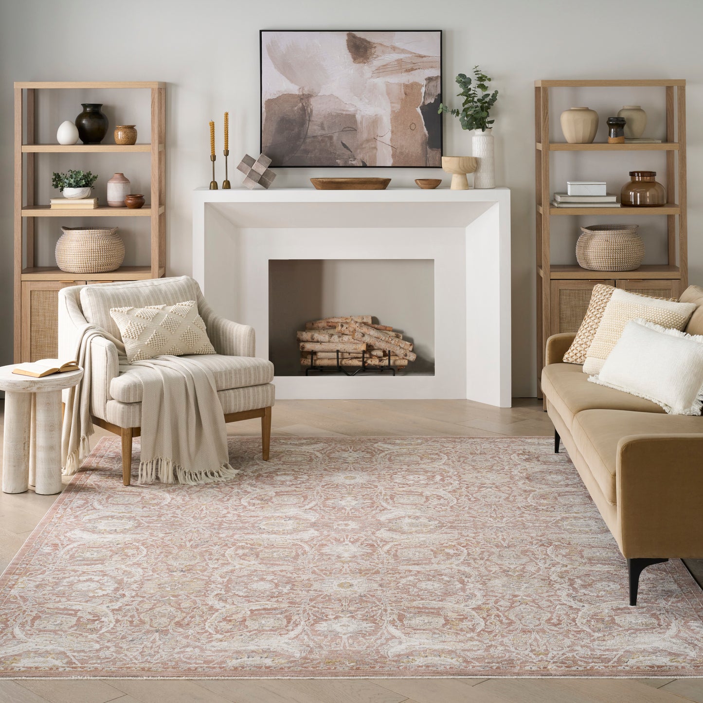 Neutral living room with beige sofa, cream armchair, light wood shelves, white fireplace, abstract art, pink patterned rug.