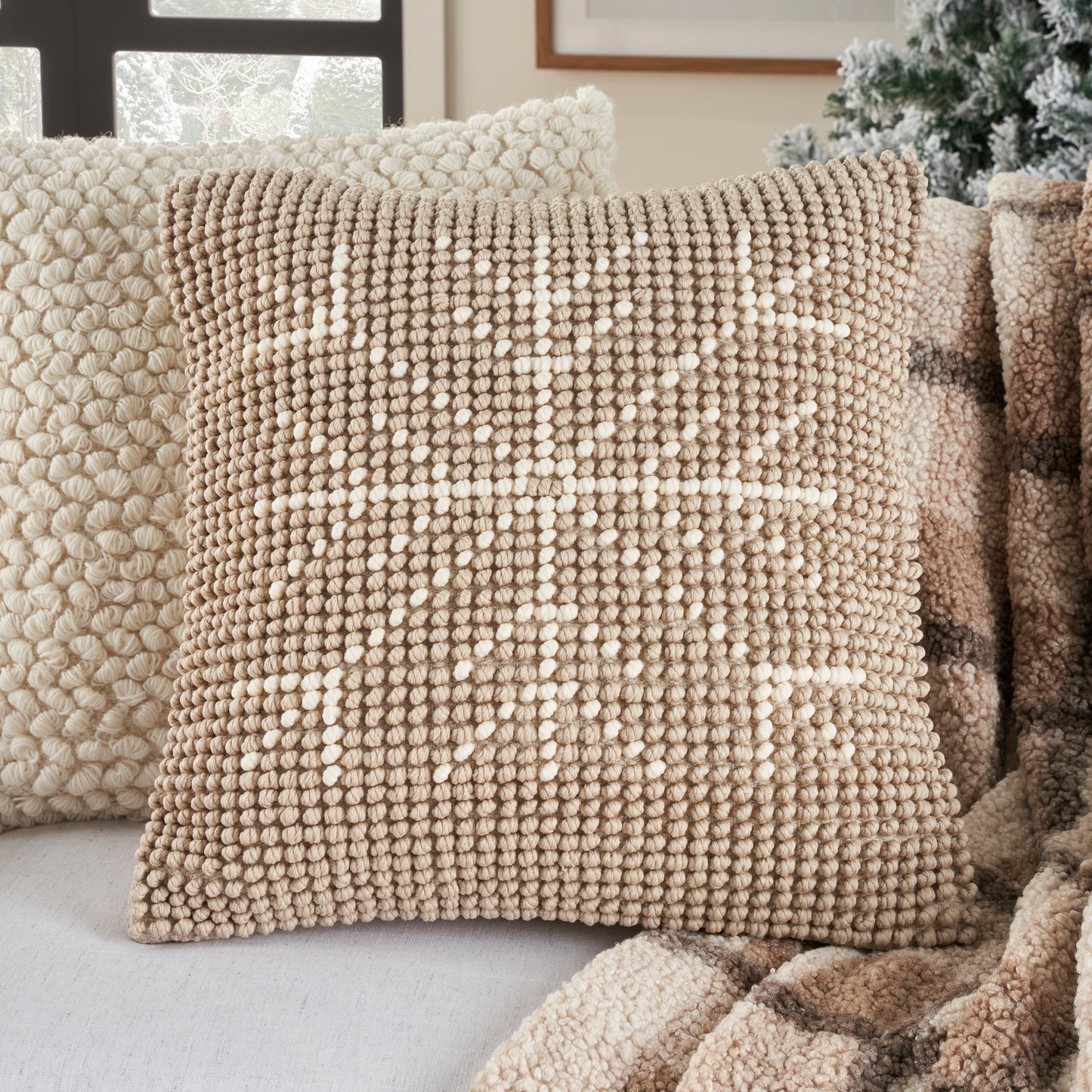 Beige boucle pillow with chunky texture and white geometric cross/star motif for cozy neutral decor