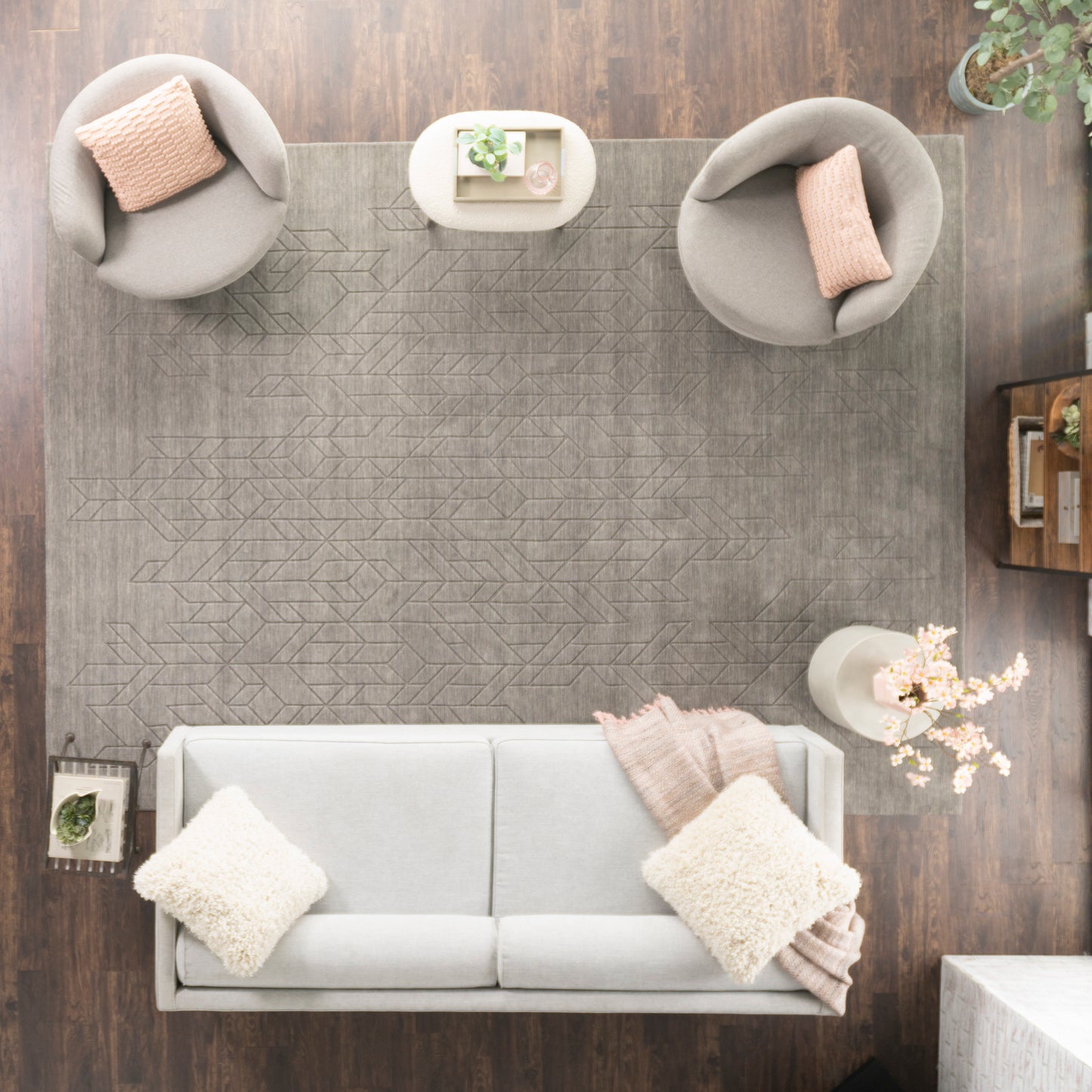 Top-down modern living room: light gray sofa with cream pillows and peach throws, round gray chairs, geometric rug.