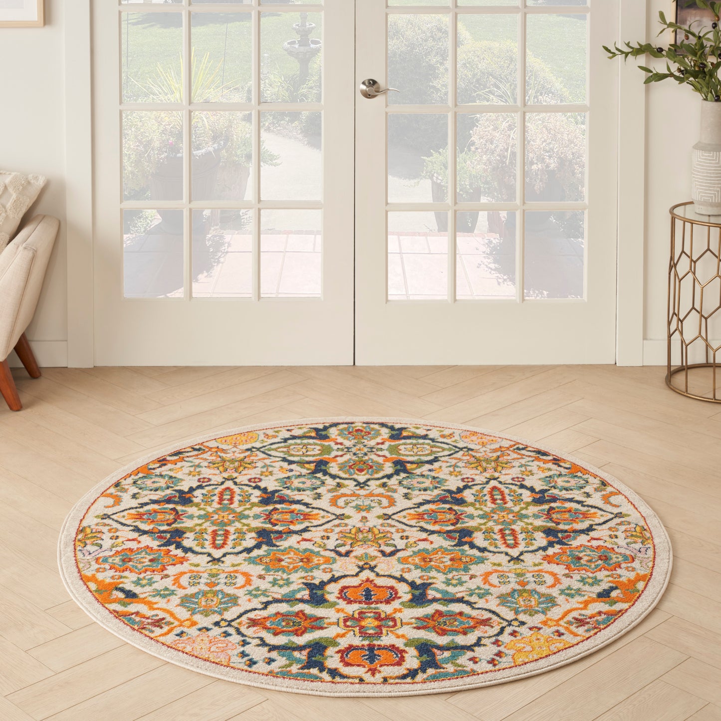 Round decorative rug with a vibrant orange, teal, navy and cream floral pattern on a light wood floor by French doors.